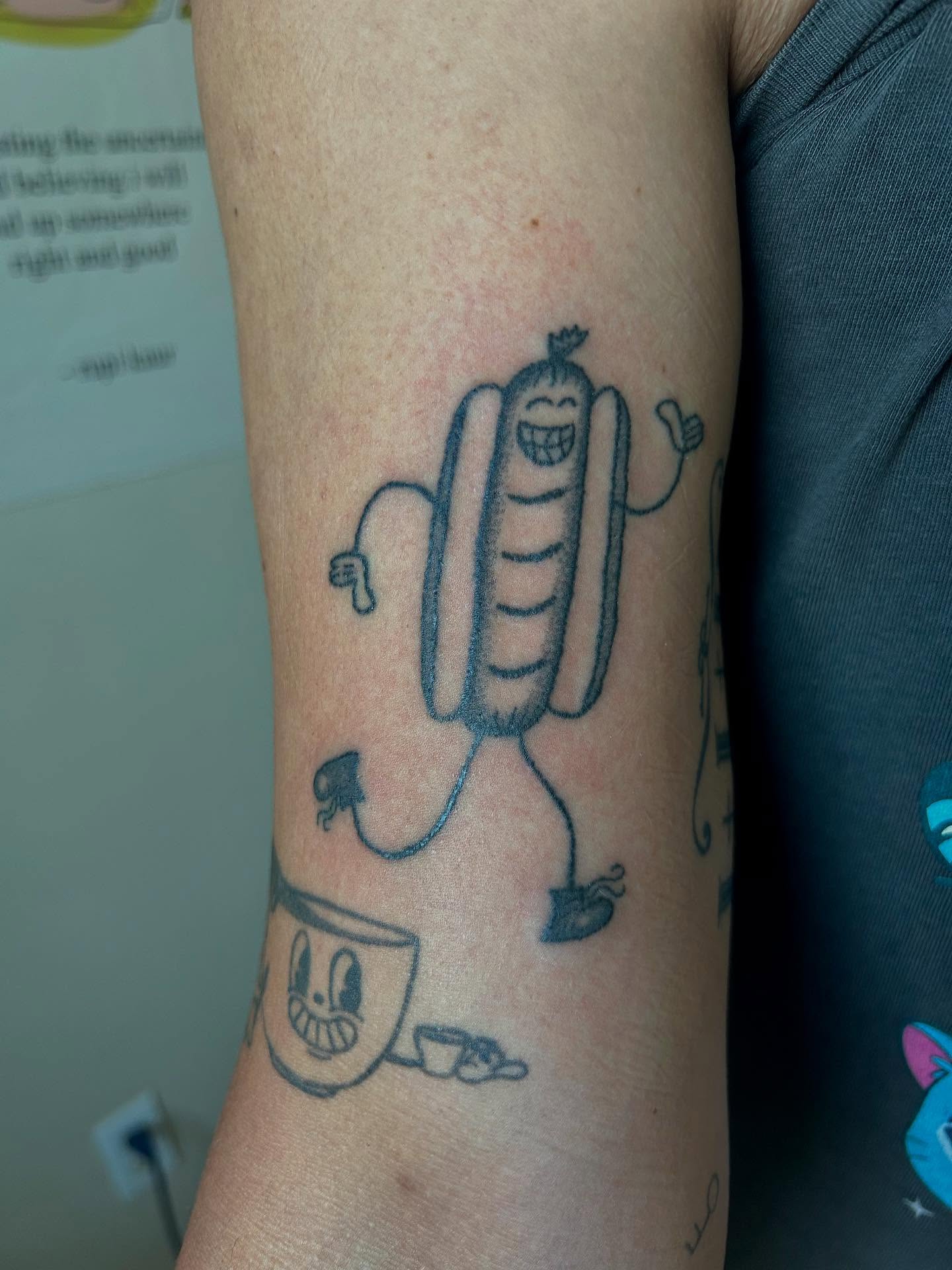 Sausage character black and grey tattoo on the forearm by Emma D