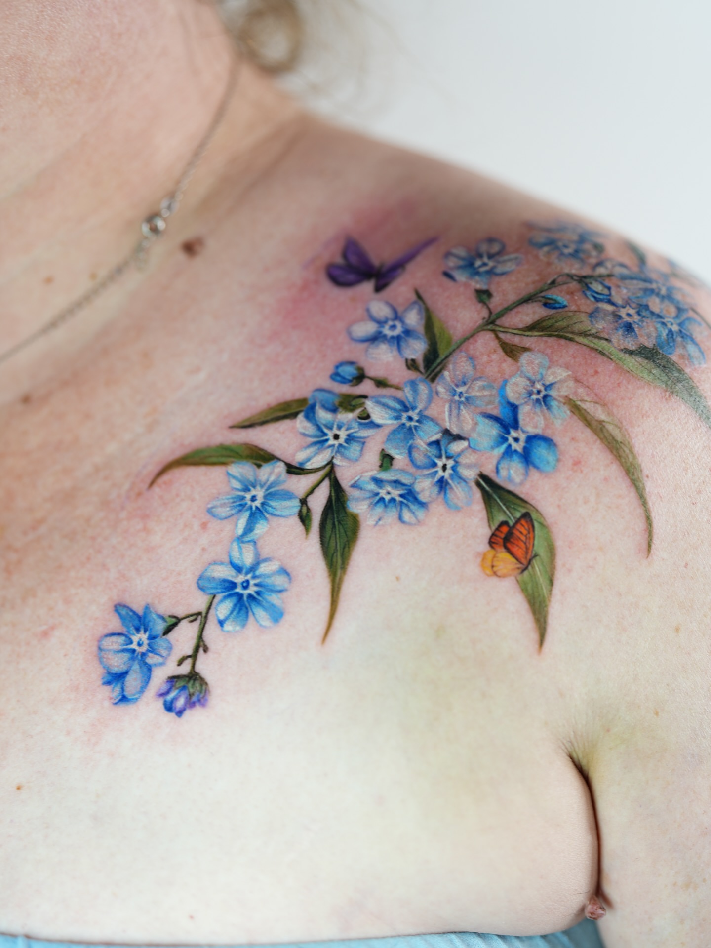 Blue forget-me-not flowers realism tattoo on the shoulder by Henry