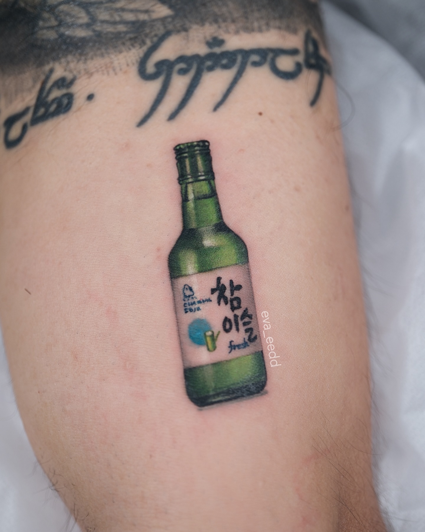 Soju bottle realism tattoo on the forearm by Eva Liu