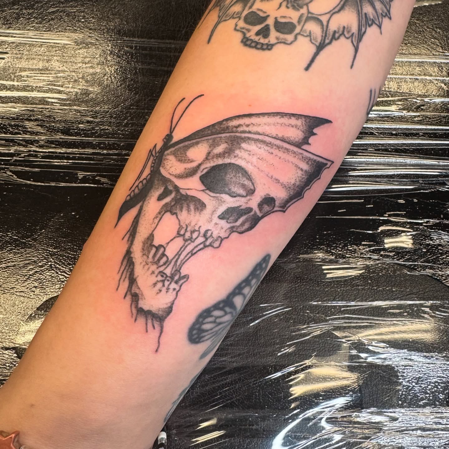 Skull with butterfly realism tattoo on the forearm by Erin Moore