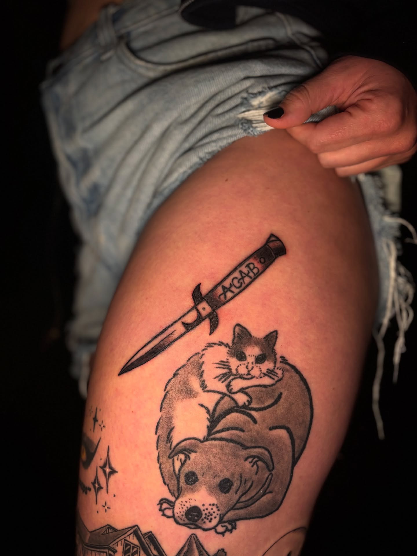 Cat and dog with knife black and grey tattoo on the thigh by Rachel