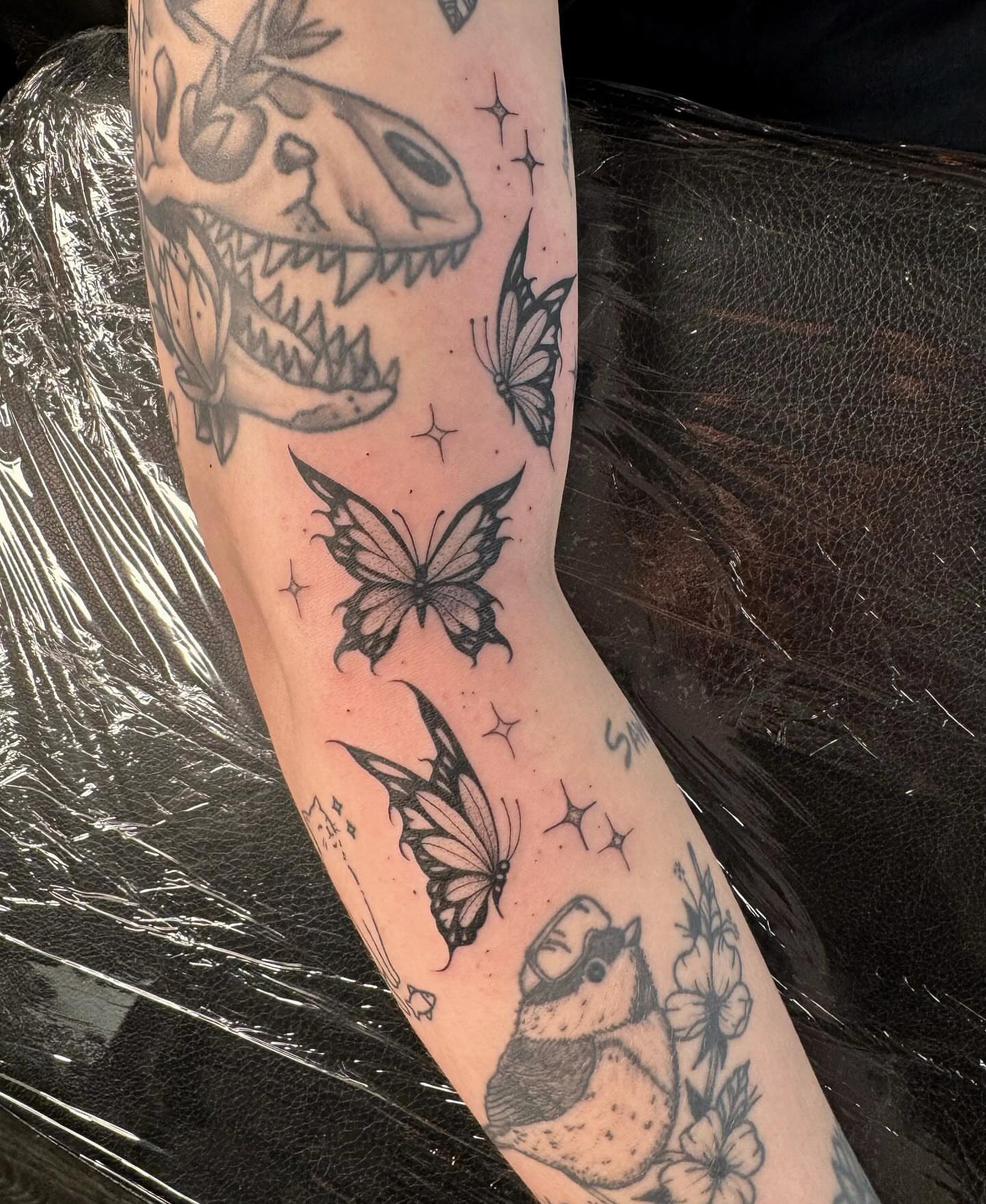 Tattooed dinosaur skull and butterflies black and grey tattoo on the forearm by Koko
