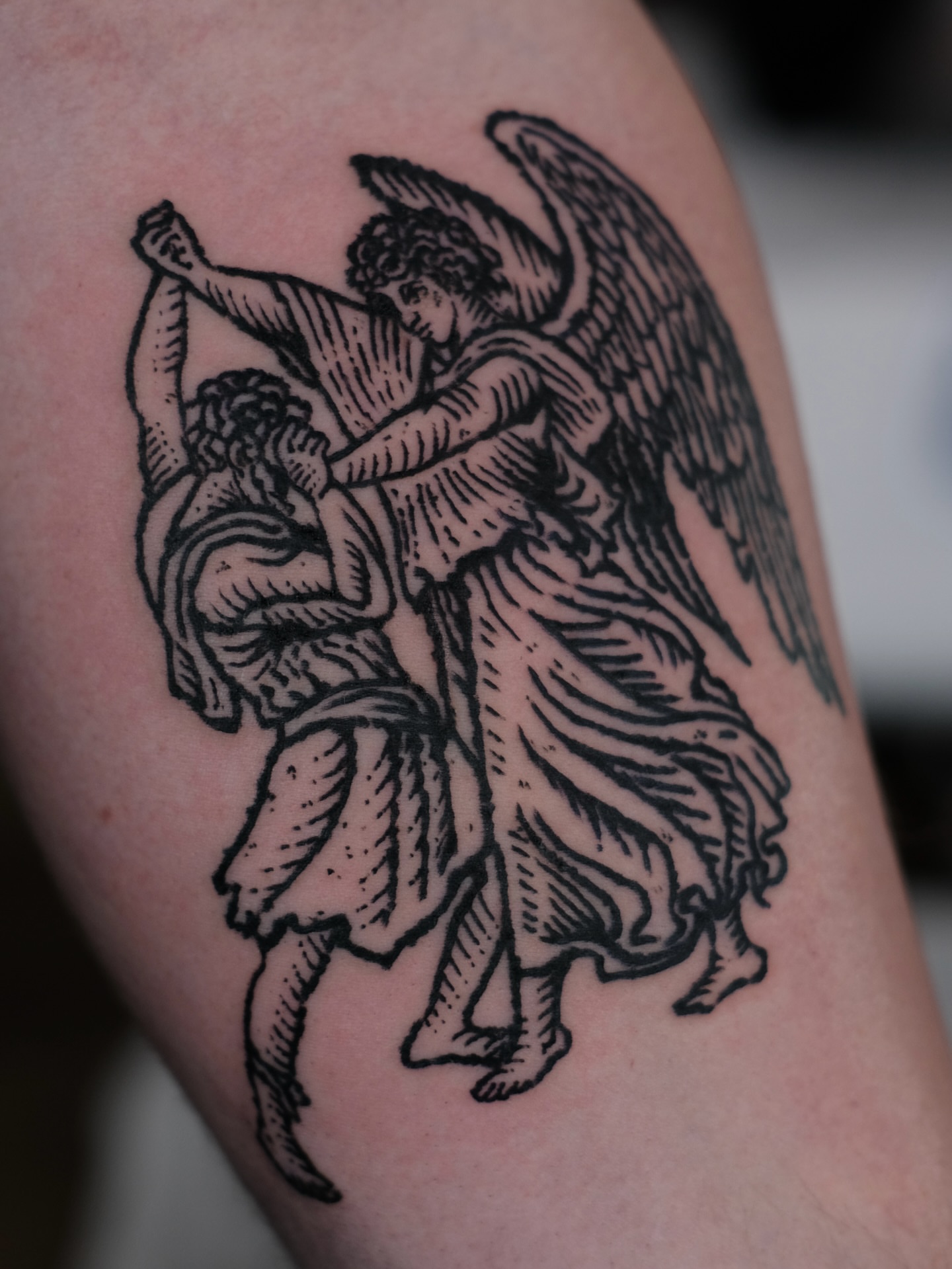 Angel carrying child black and grey tattoo on the thigh by ꜰʟᴏʀᴀ ᴡᴏᴏᴅᴄᴜᴛ ᴛᴀᴛᴛᴏᴏ