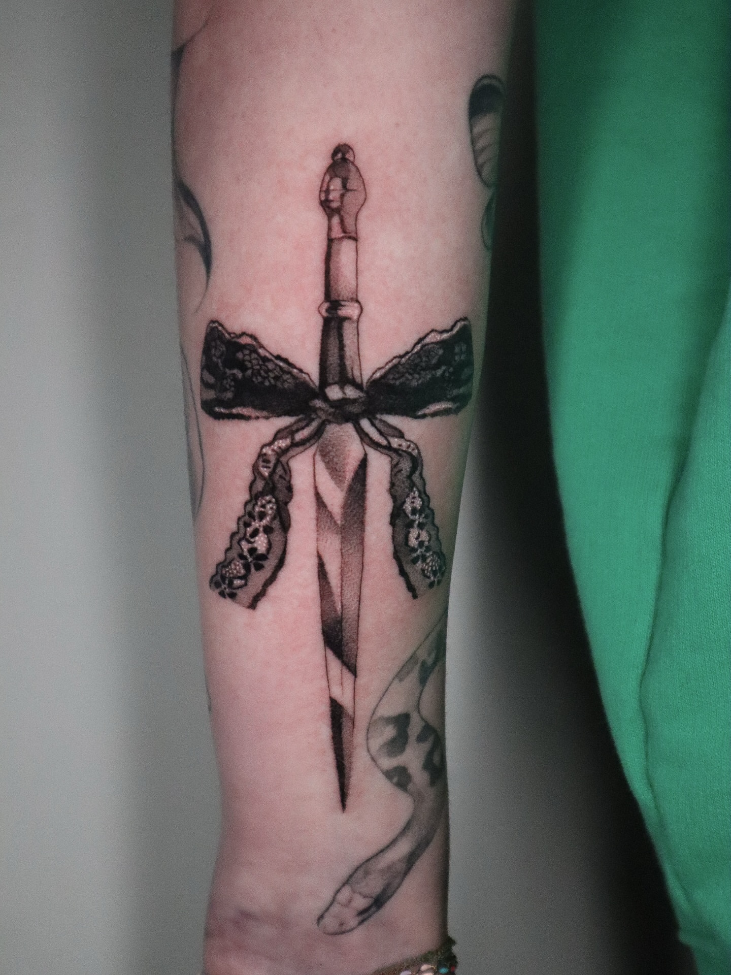 Sword with lace bow black and grey tattoo on the forearm by 𝕮𝖔𝖓𝖓𝖔𝖗 ☾  ~ TATTOO ARTIST