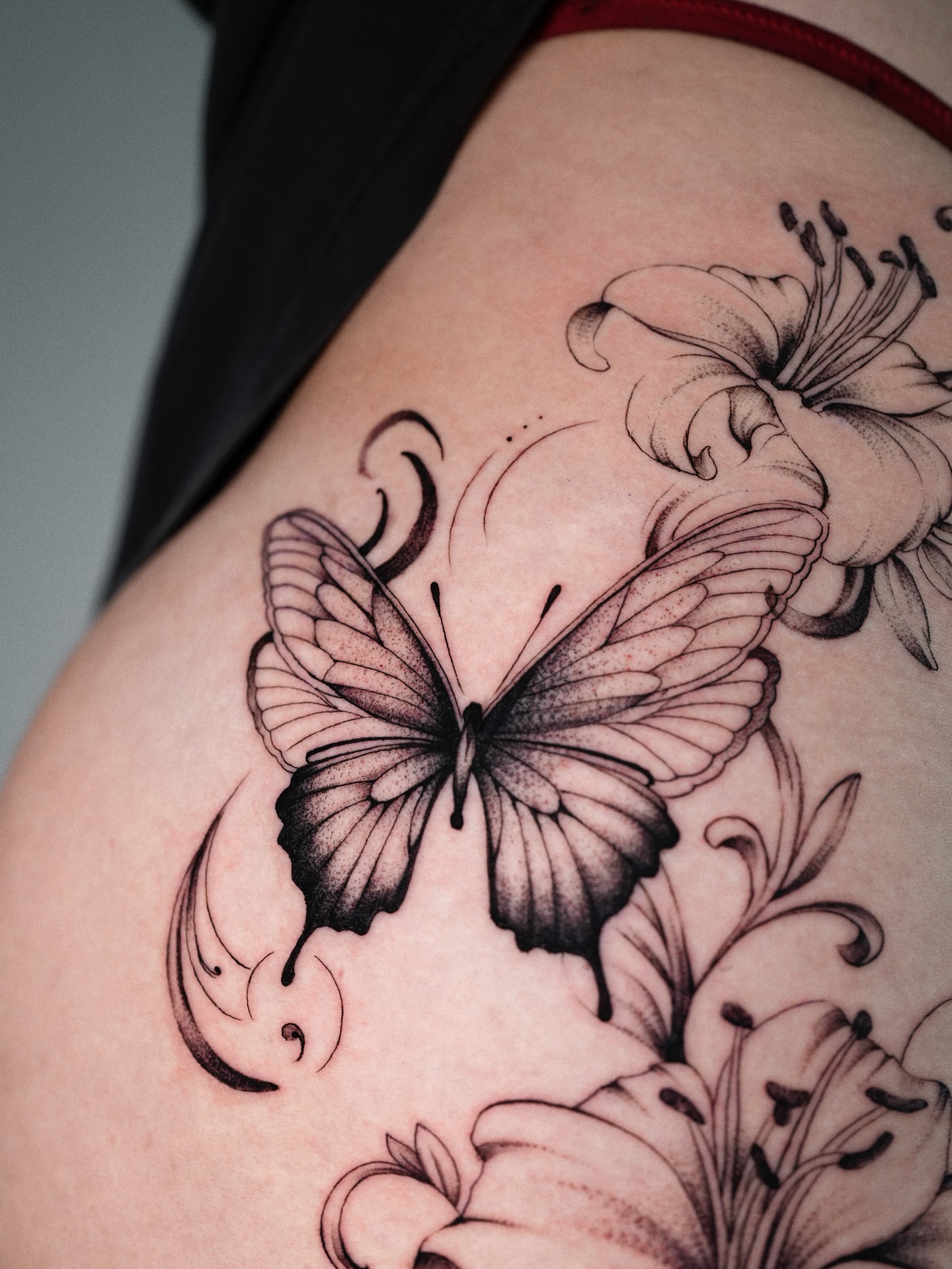 Butterfly and lily black and grey tattoo on the thigh by @katuvetattoo