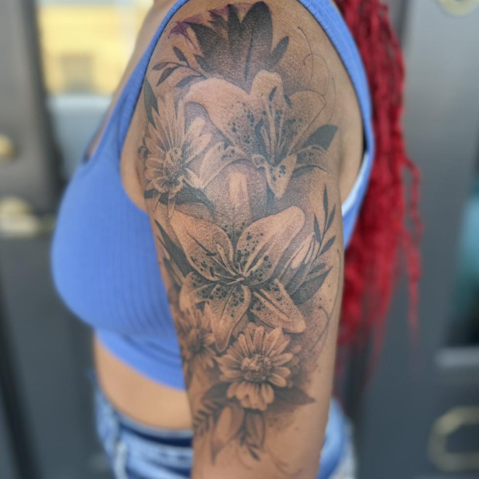 Lilies and daisies black and grey tattoo on the upper arm by Tattoos by Aeron Herald Maurbjorn, Sioux