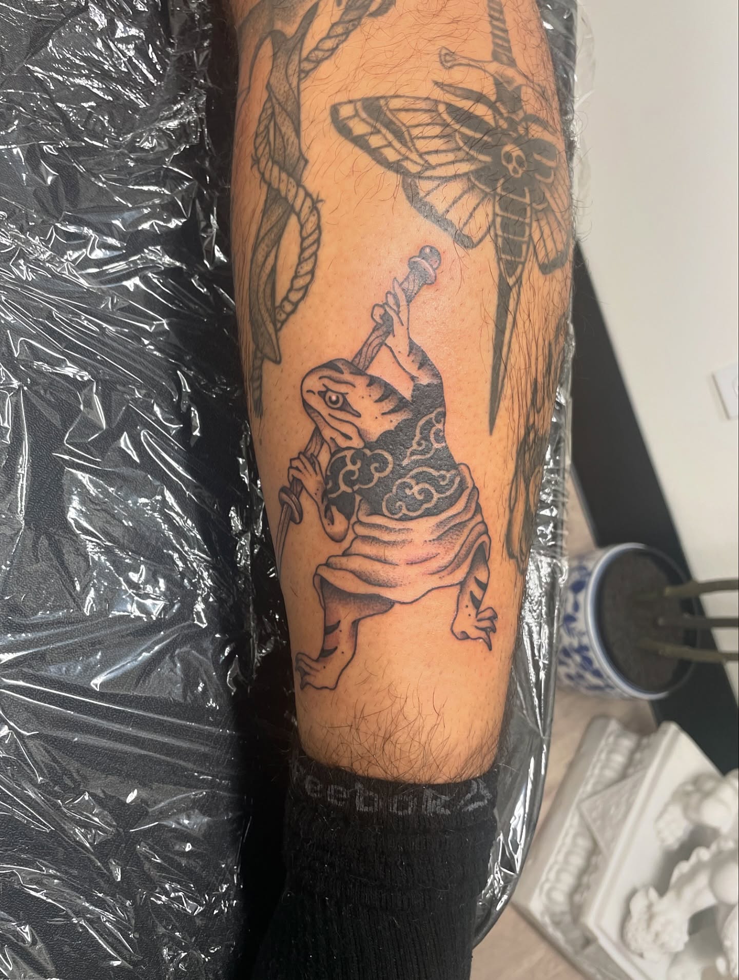 Frog with staff black and grey tattoo on the forearm by 𝕯𝖔𝖒