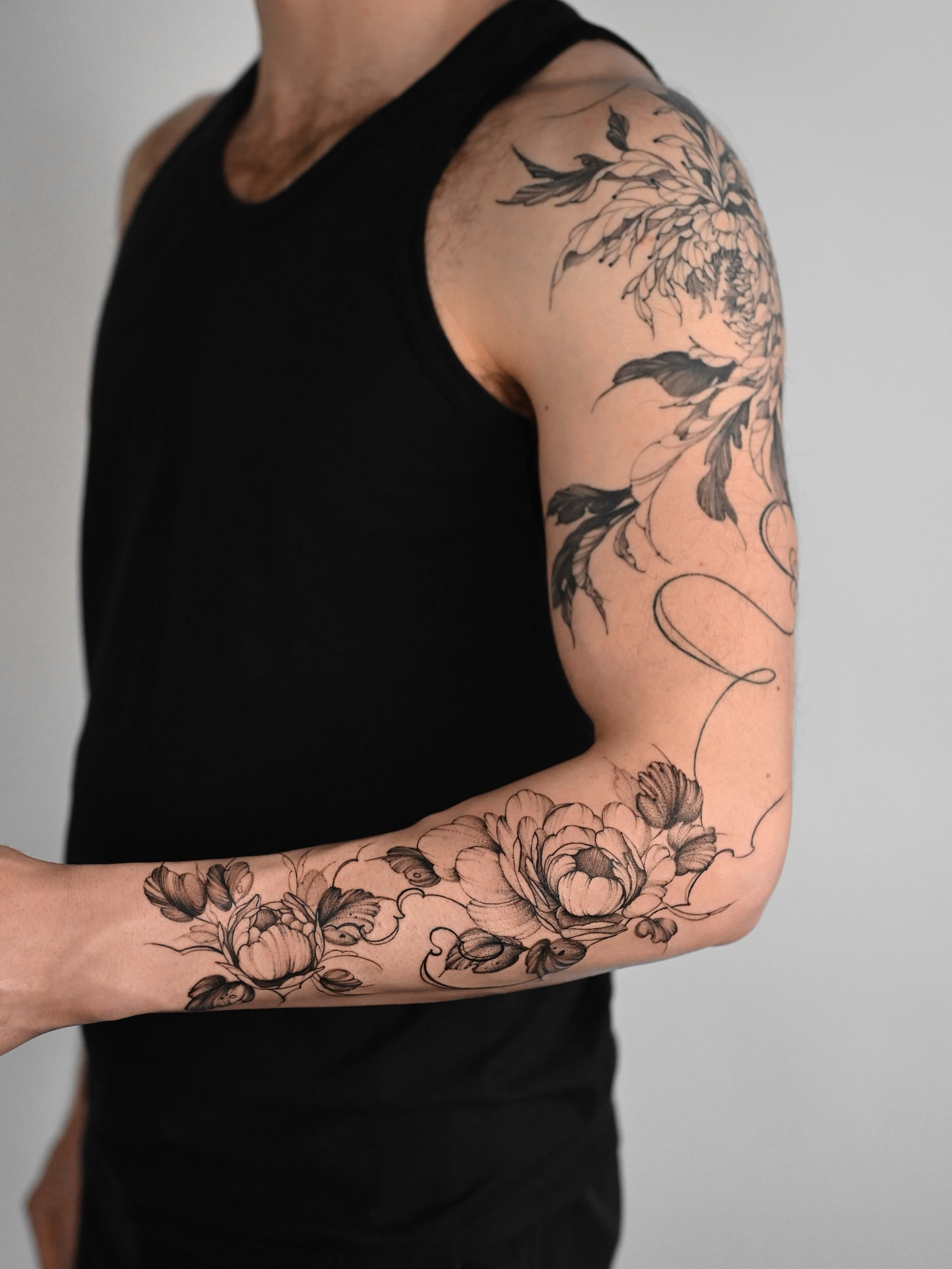 Floral black and grey tattoo on the upper arm by Anastasiia