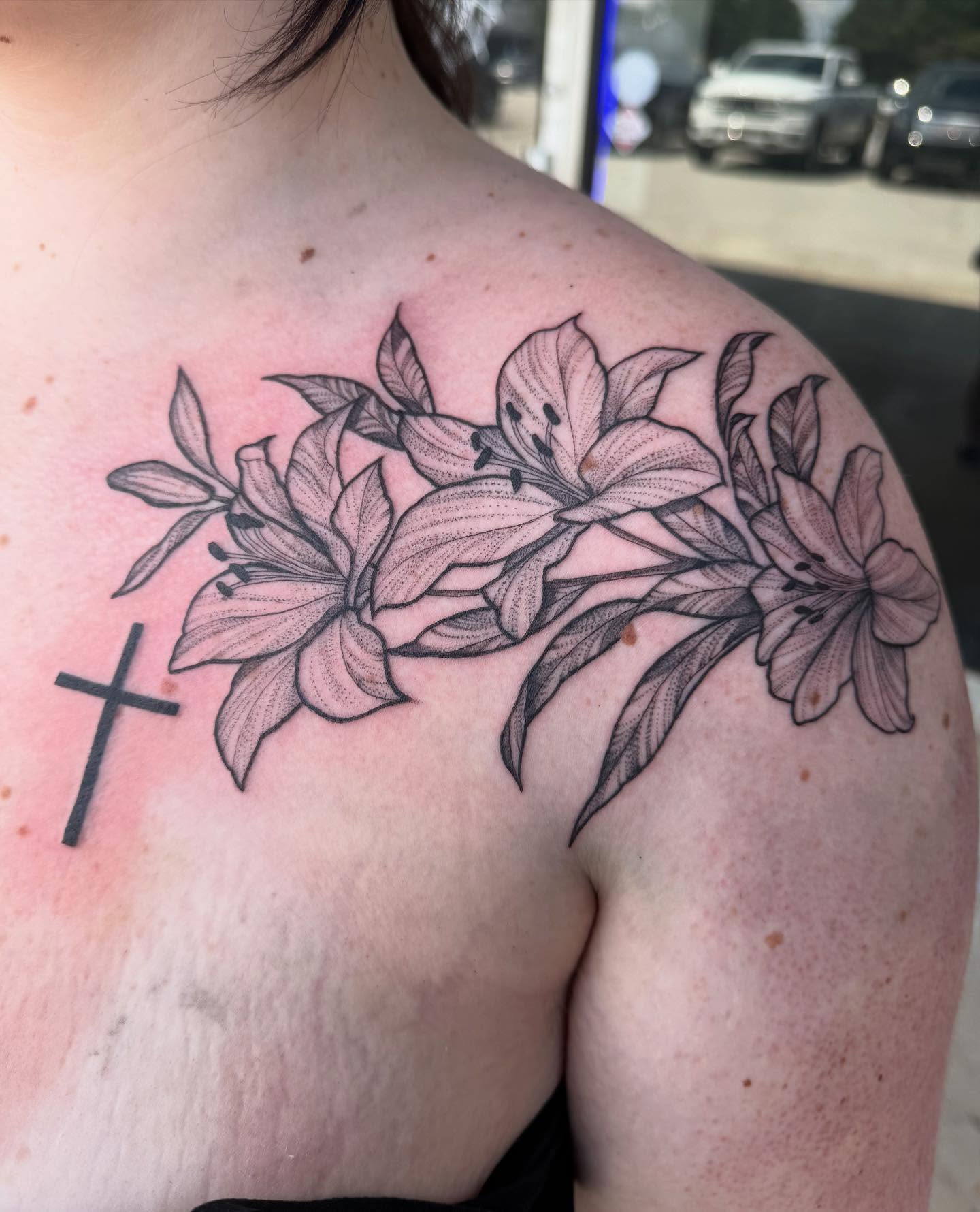 Lilies and cross black and grey tattoo on the shoulder by Ashley matthews