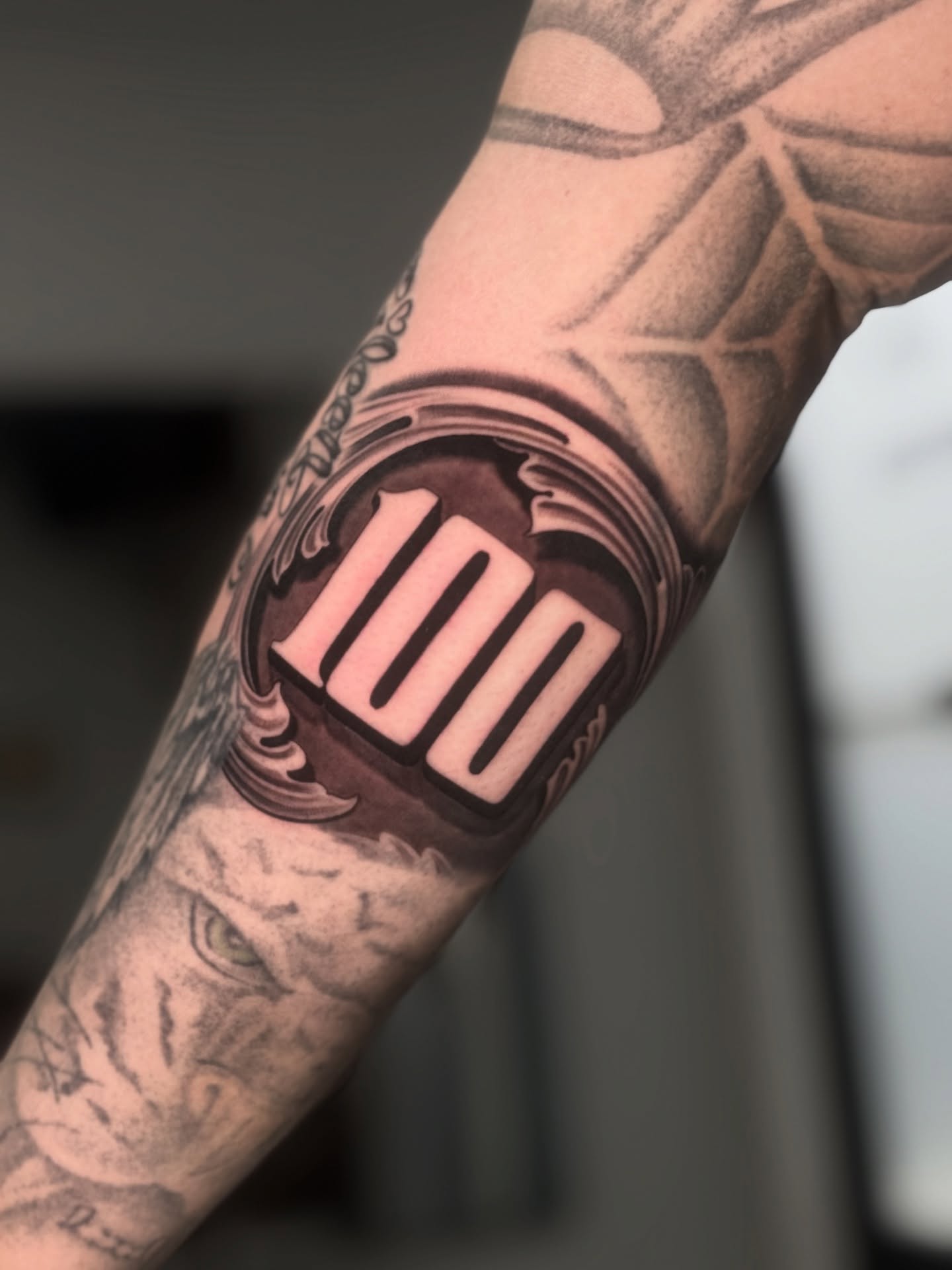 Number 100 black and grey tattoo on the forearm by Sergio Mendez