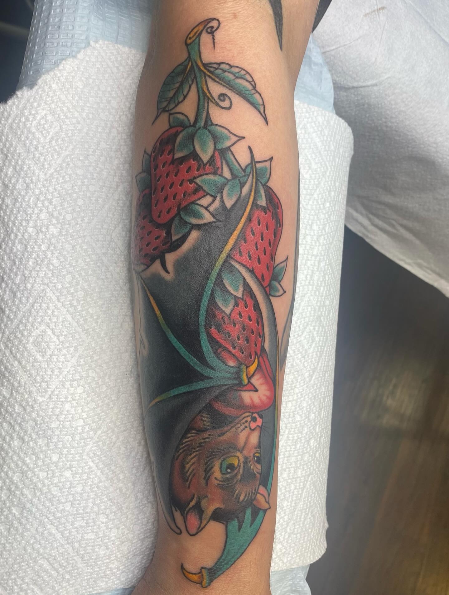 Strawberries and cat American traditional tattoo on the forearm by Thomas Cook