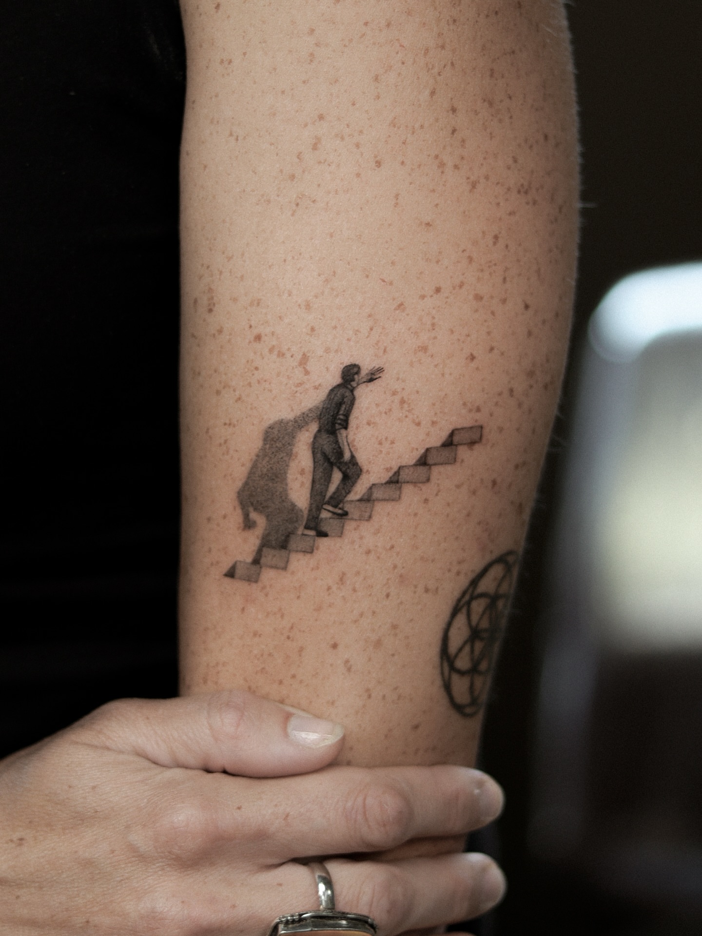 Man climbing stairs black and grey tattoo on the forearm by Arthur Kossoski