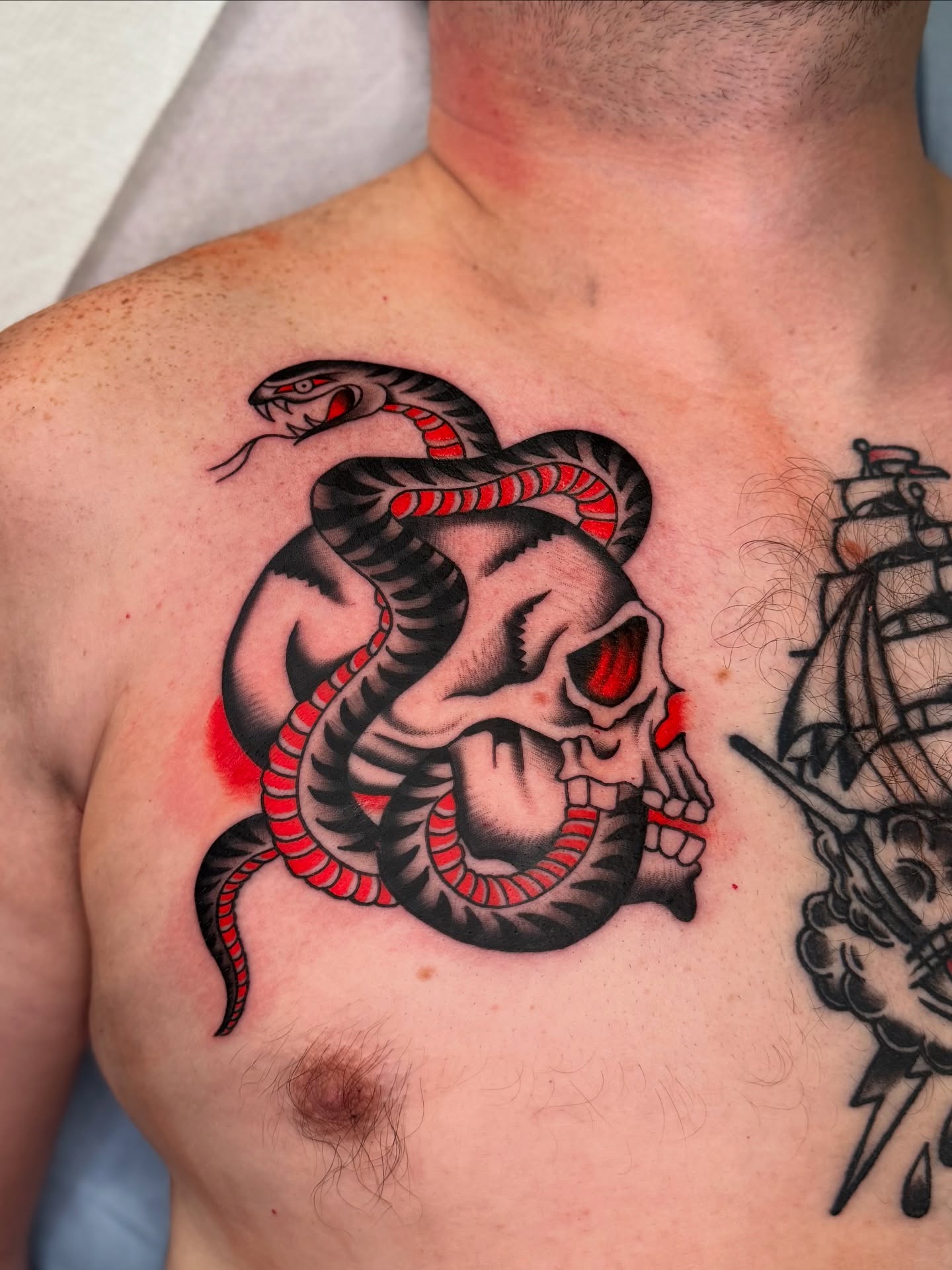Snake and skull American traditional tattoo on the chest by Allie Barringer
