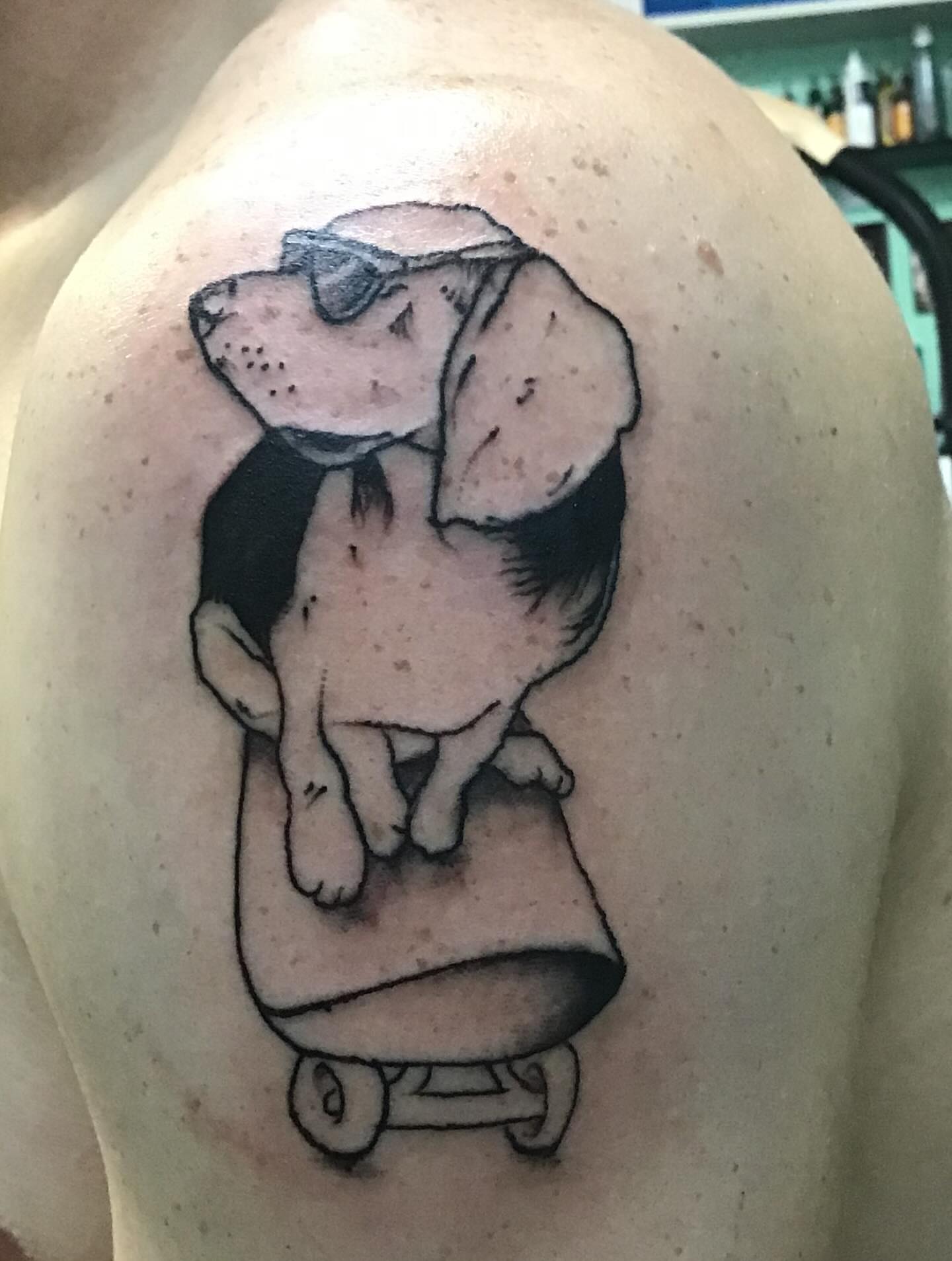 Dog on skateboard black and grey tattoo on the shoulder by Roachrude