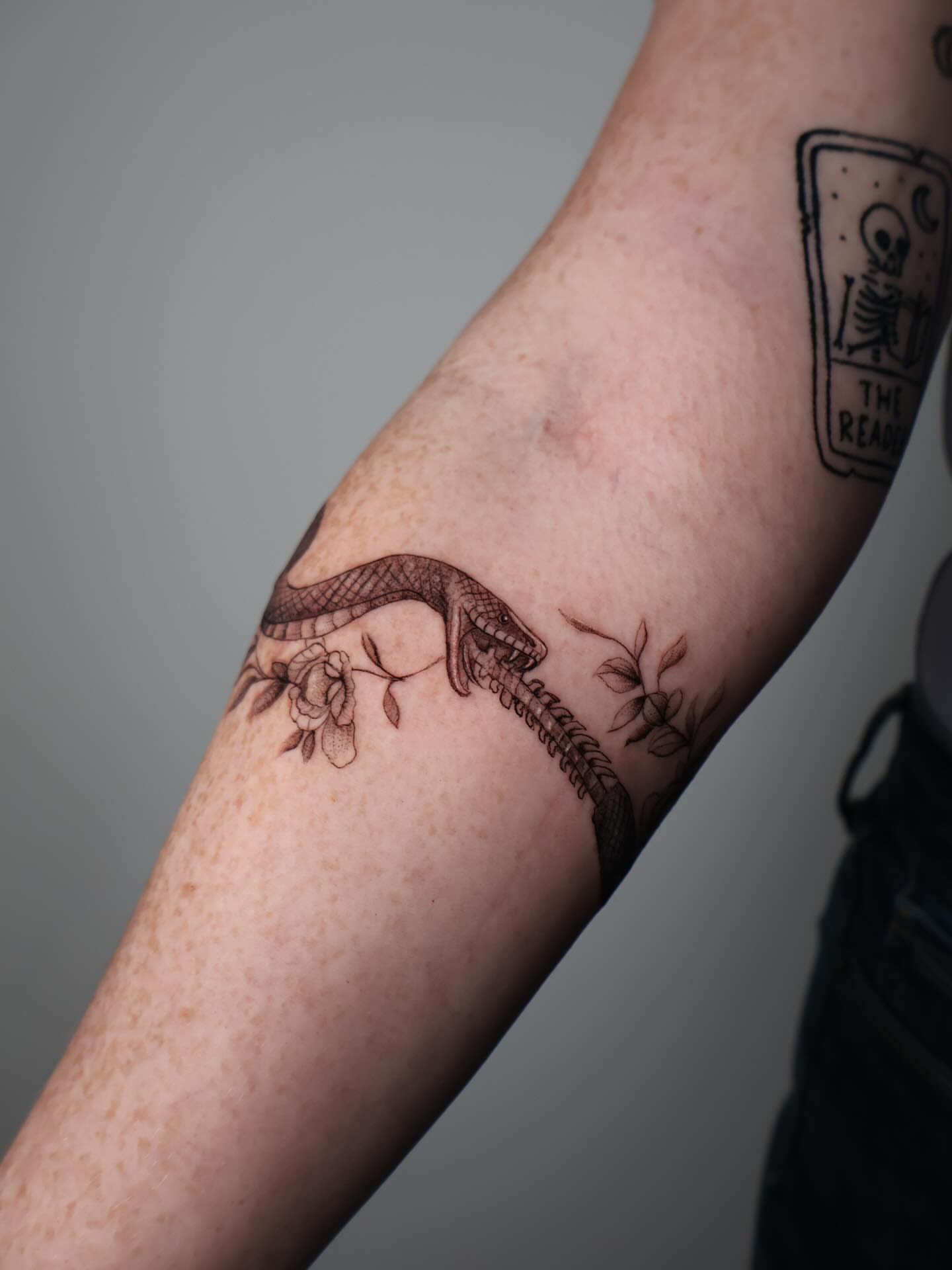 Snake and flowers black and grey tattoo on the forearm by Stephanie Pedraza