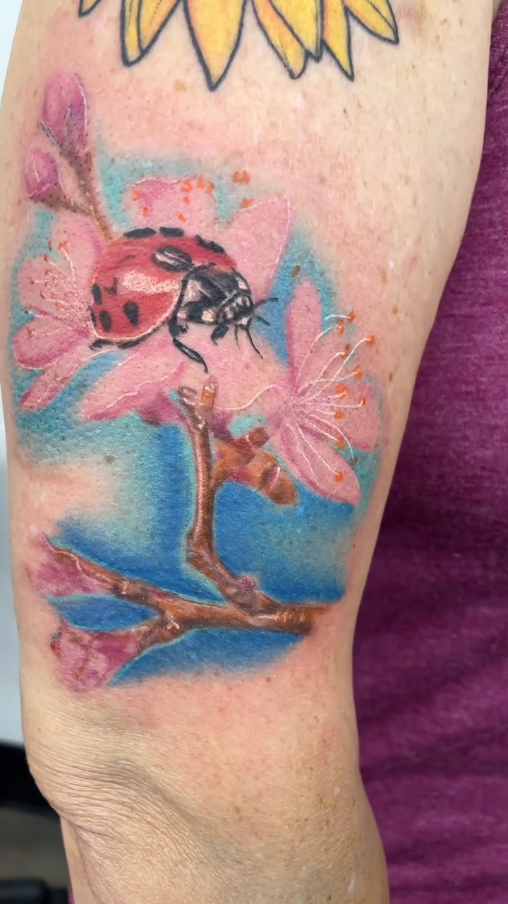 Ladybug on a branch with flowers realism tattoo by Cultura