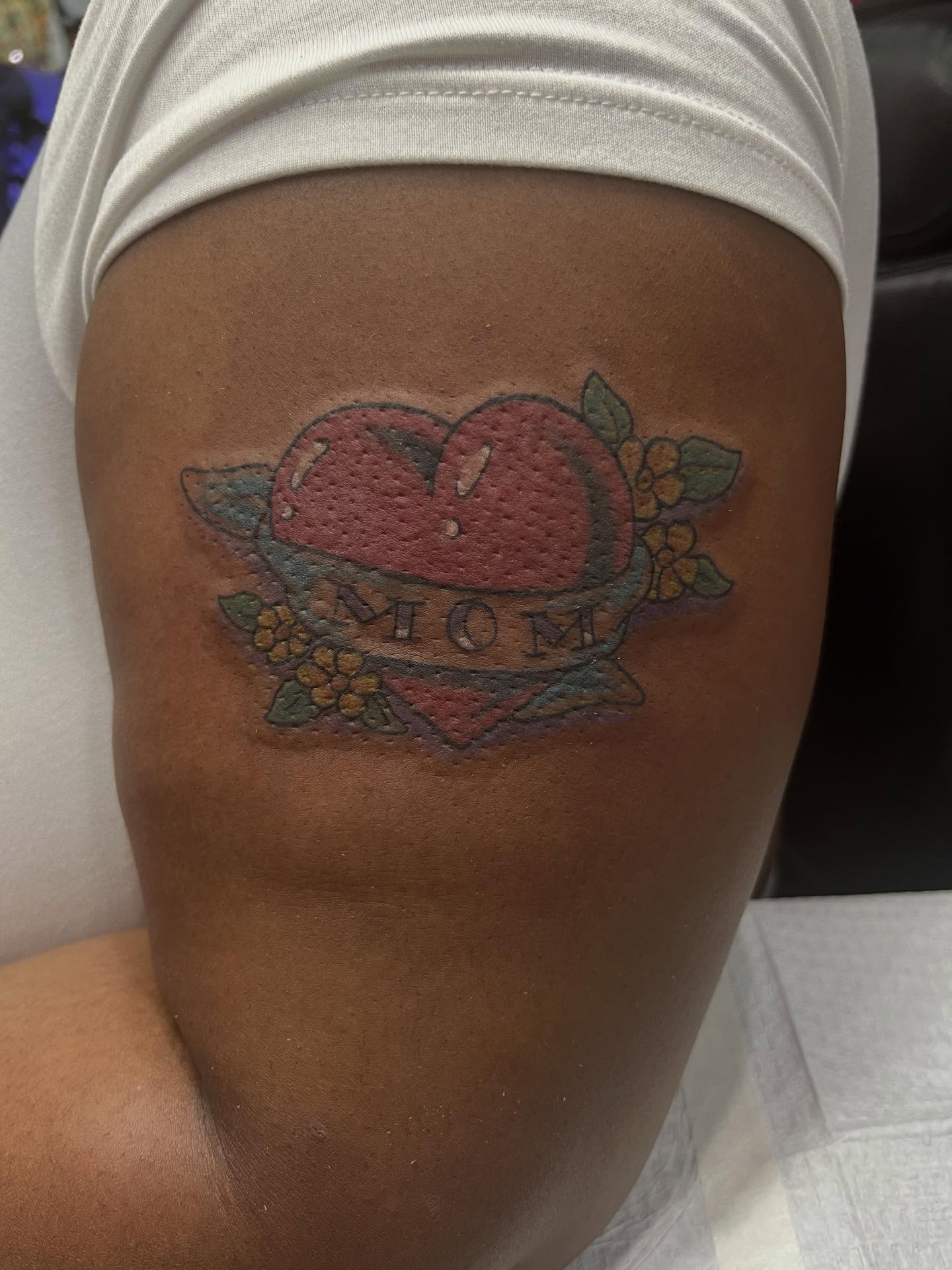 Heart with 'mom' American traditional tattoo on the thigh by Kenny Buck