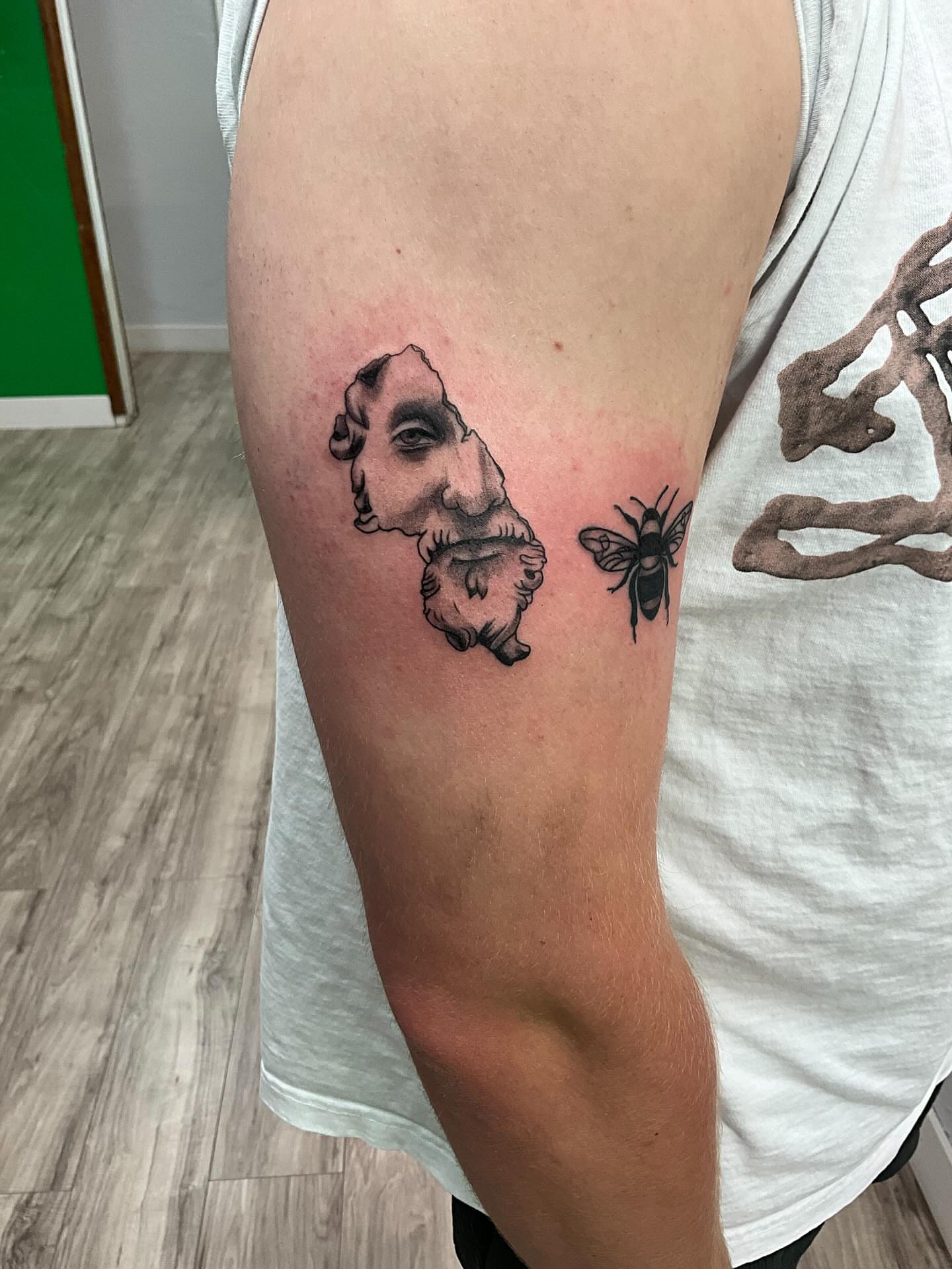 Statue head and bee black and grey tattoo on the forearm by James Ostler