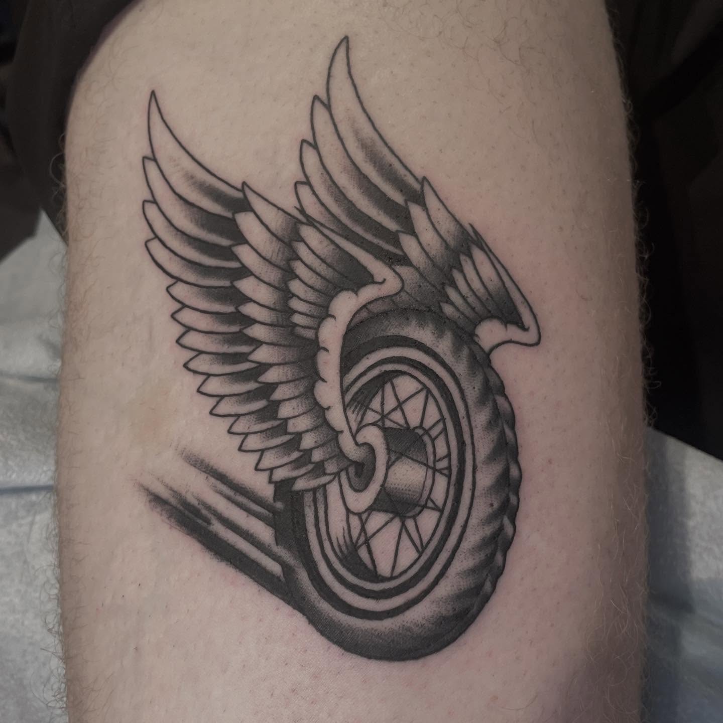 Motorcycle wheel with wings black and grey tattoo on the thigh by Amanda Marie, Edmonds, Washington