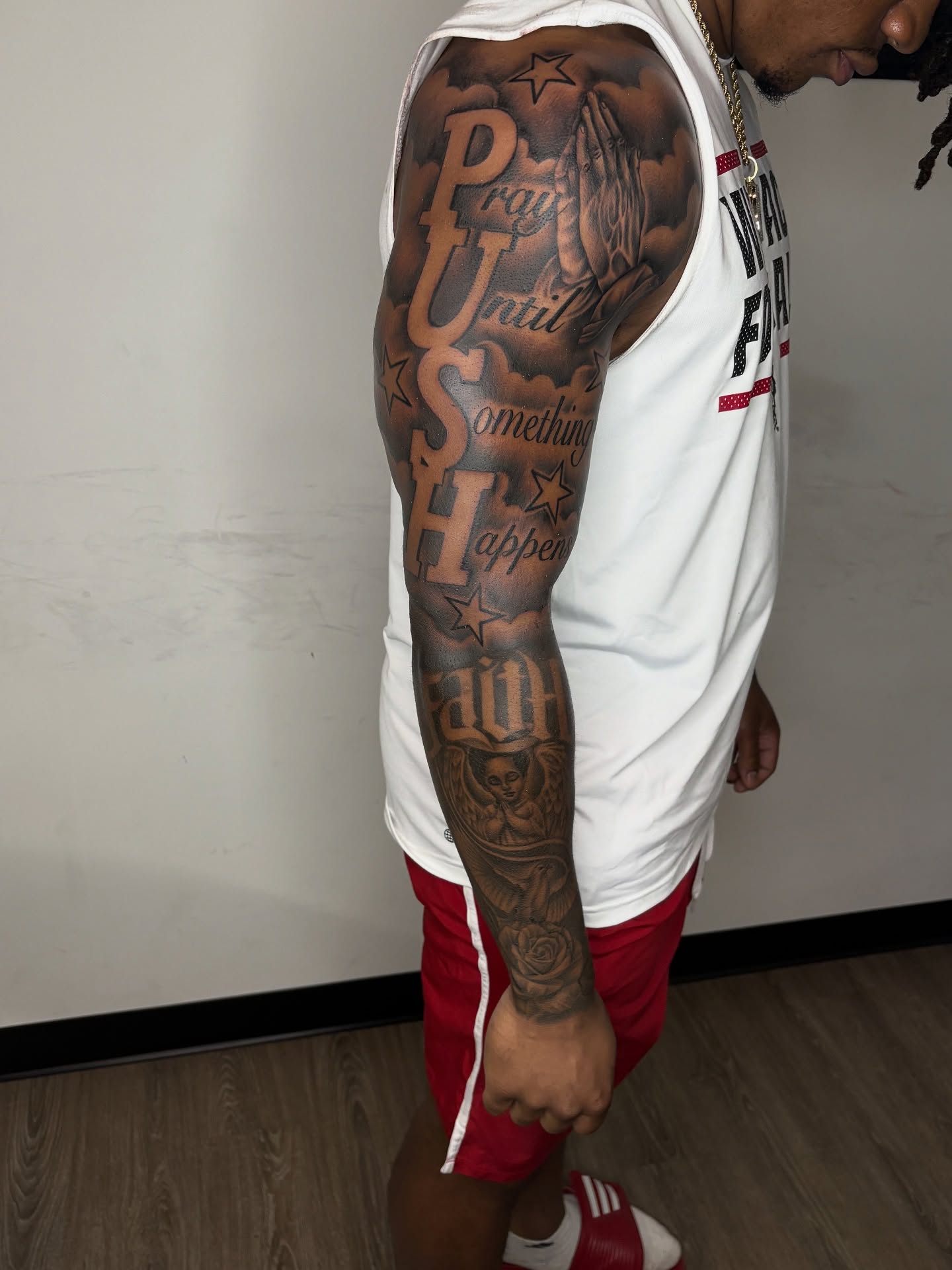 Prayer hands and motivational text black and grey tattoo on the upper arm by Vonte Seay