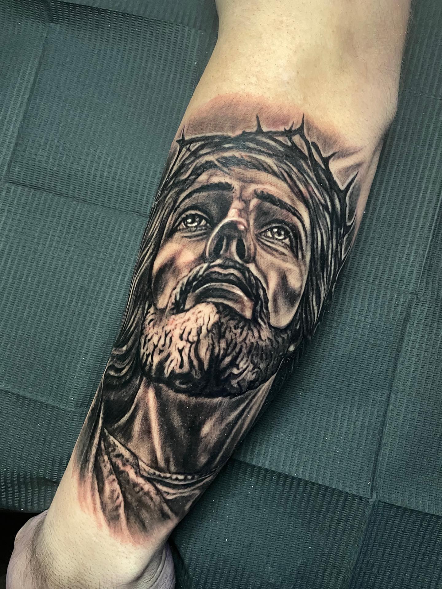Religious figure realism tattoo on the forearm by Rick Elliott