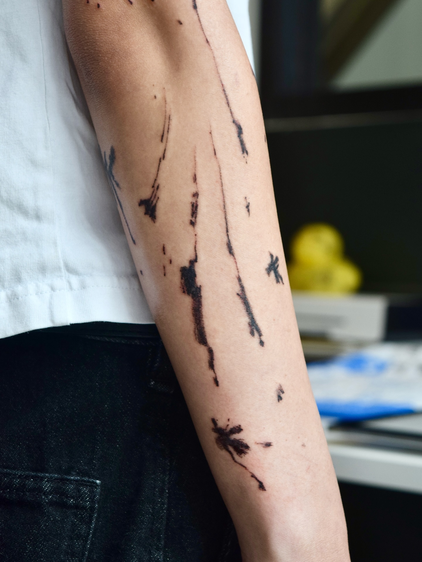Ink splatters black and grey tattoo on the forearm by Stella Oh