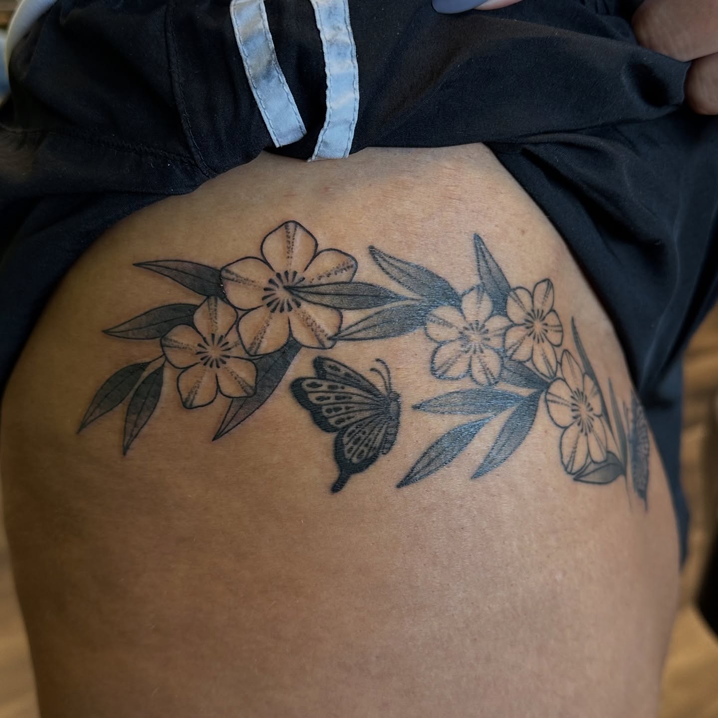 Flowers and butterfly black and grey tattoo on the thigh by Lauren Howard Tattoos
