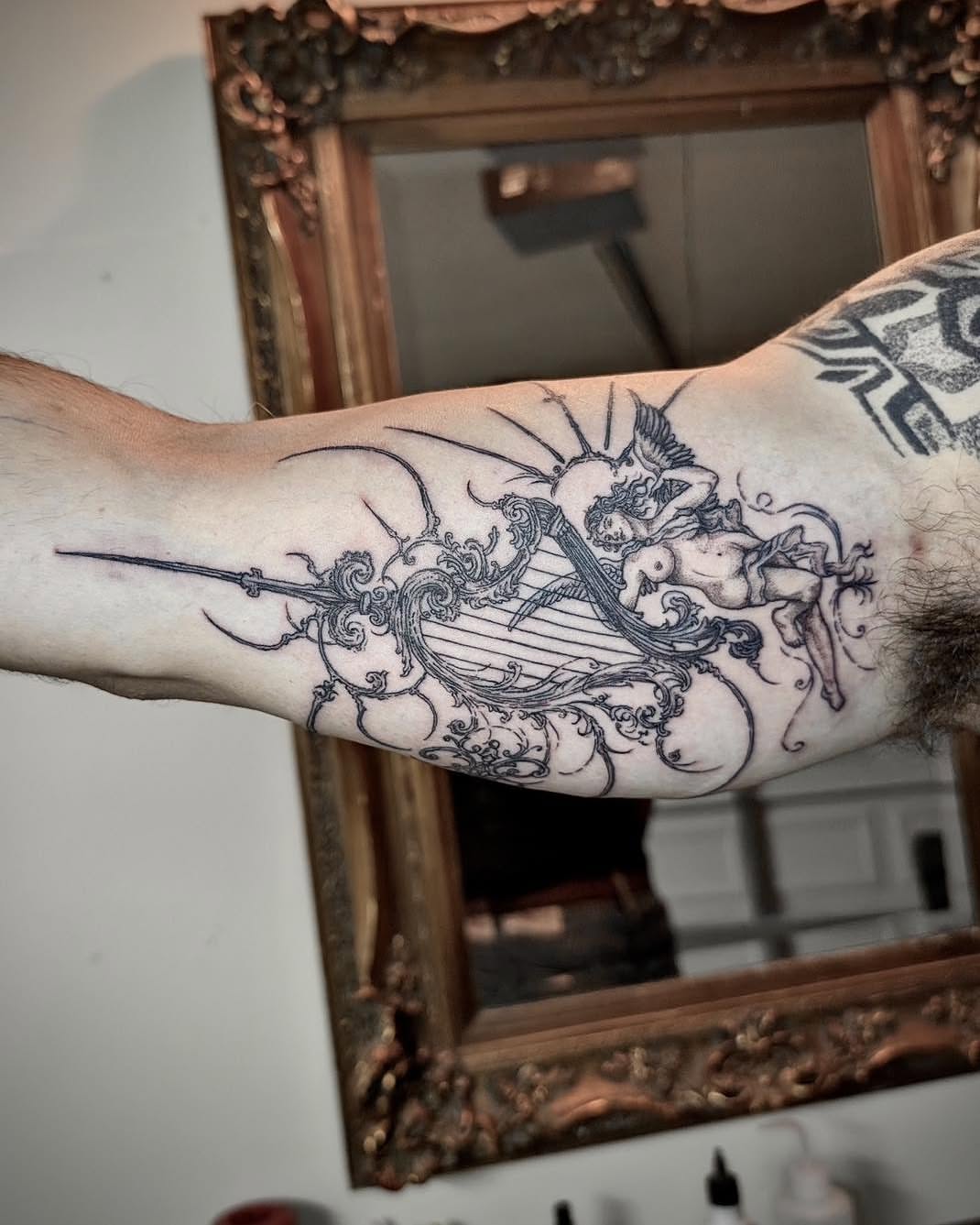 Cherub and harp black and grey tattoo on the forearm by Quin Walker