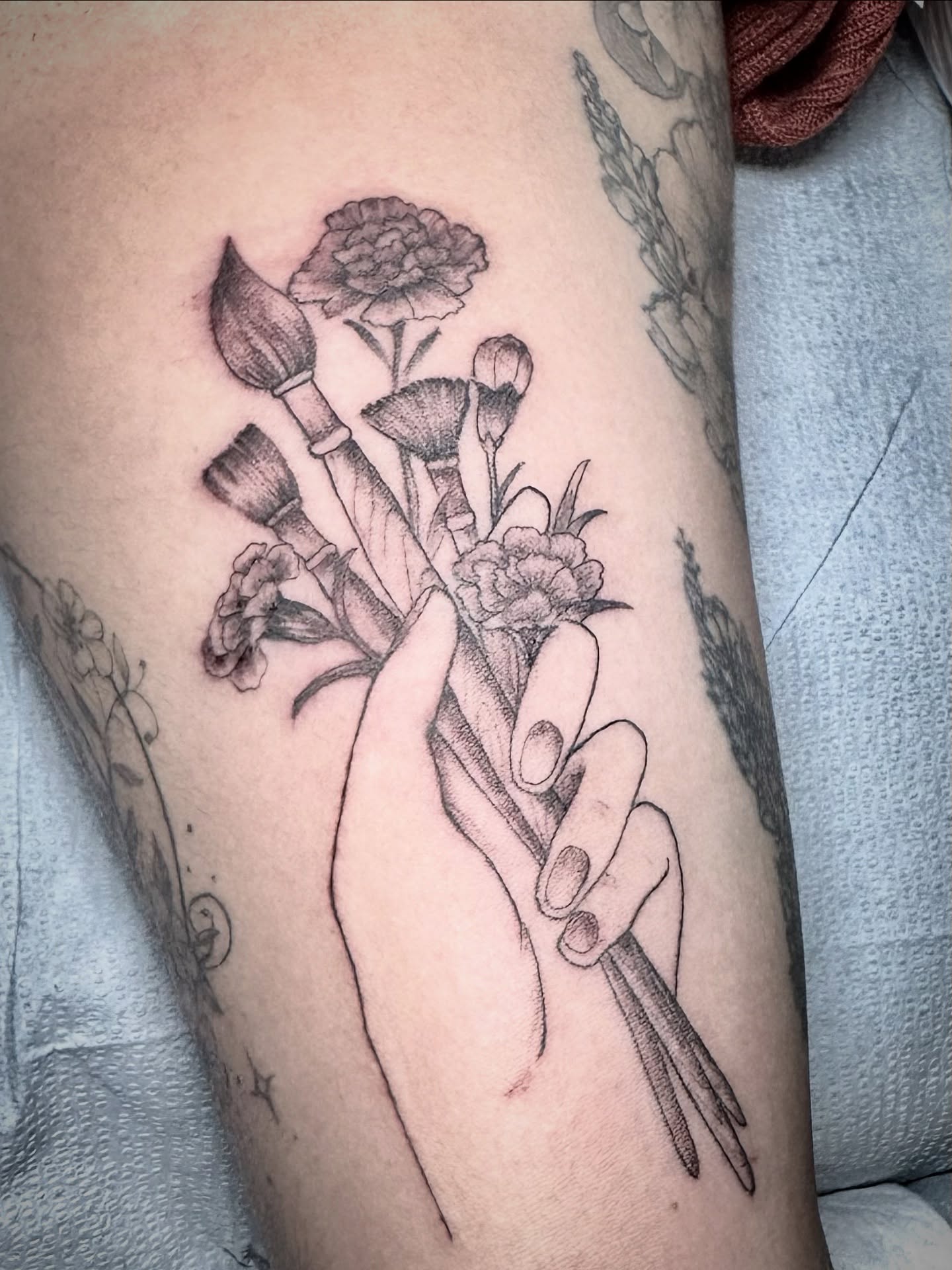 Hand holding flowers black and grey tattoo on the forearm by đź’›Kristinađź’› tattoos with intention, Minneapolis, Minnesota