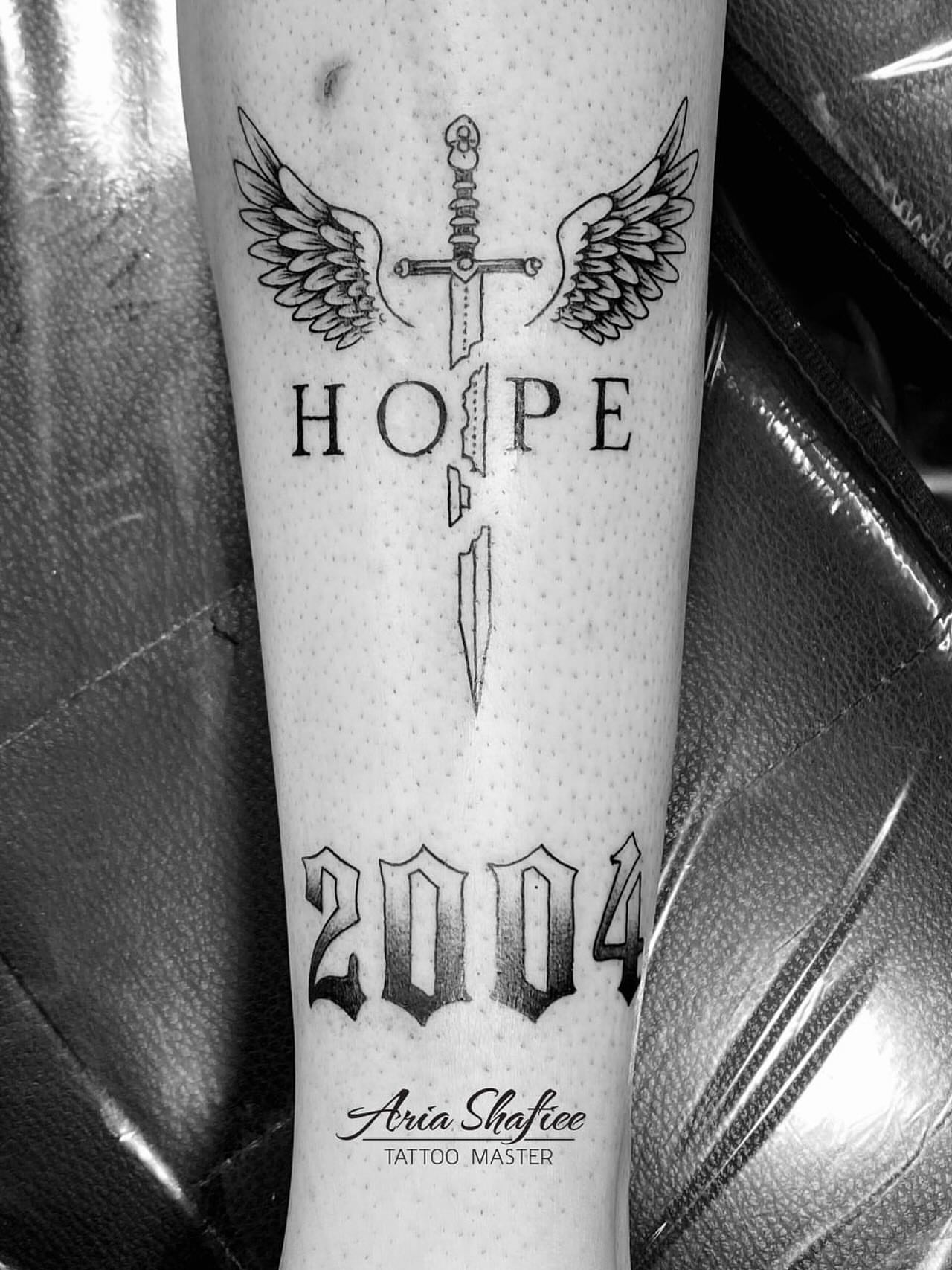 Sword with wings black and grey tattoo on the forearm by Aria Shafiee