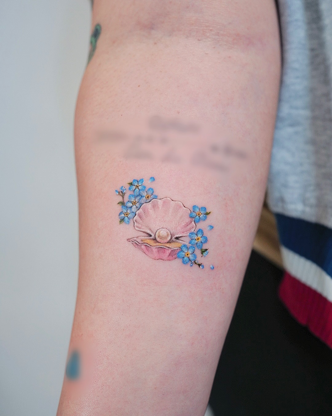 Shell and flowers watercolor tattoo on the forearm by Lily, Los Angeles, California