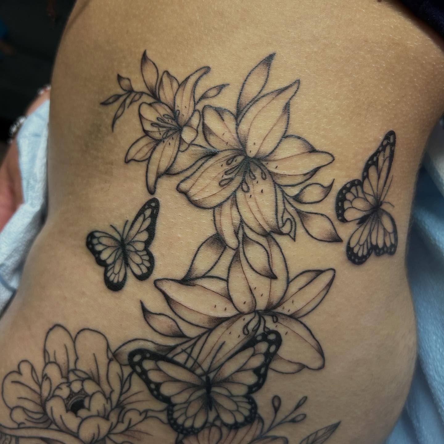 Lilies and butterflies black and grey tattoo on the thigh by Kells