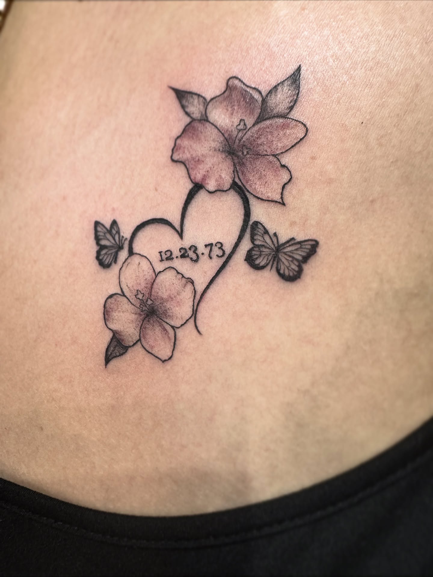 Heart with flowers and butterflies black and grey tattoo on the ribs by Christa Martinez