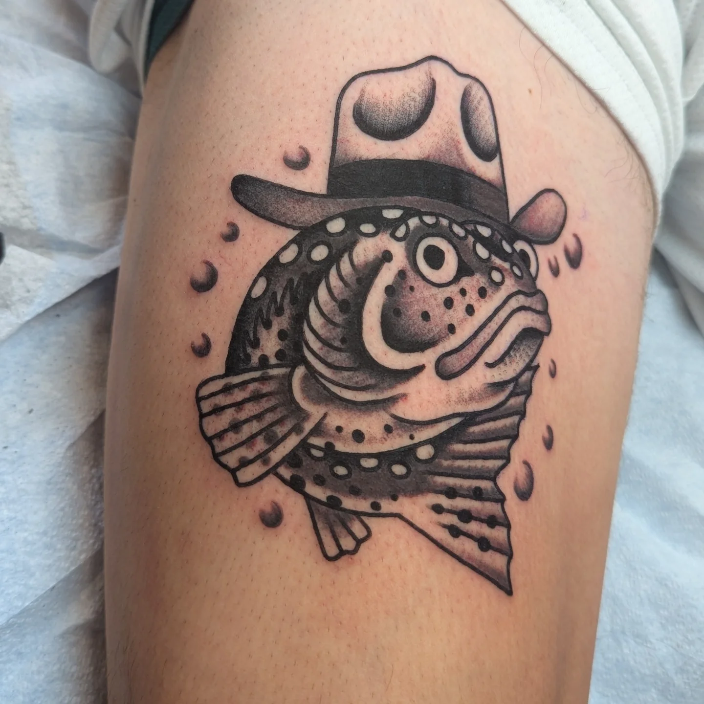 Fish wearing a hat dotwork tattoo on the thigh by Zack Mueller