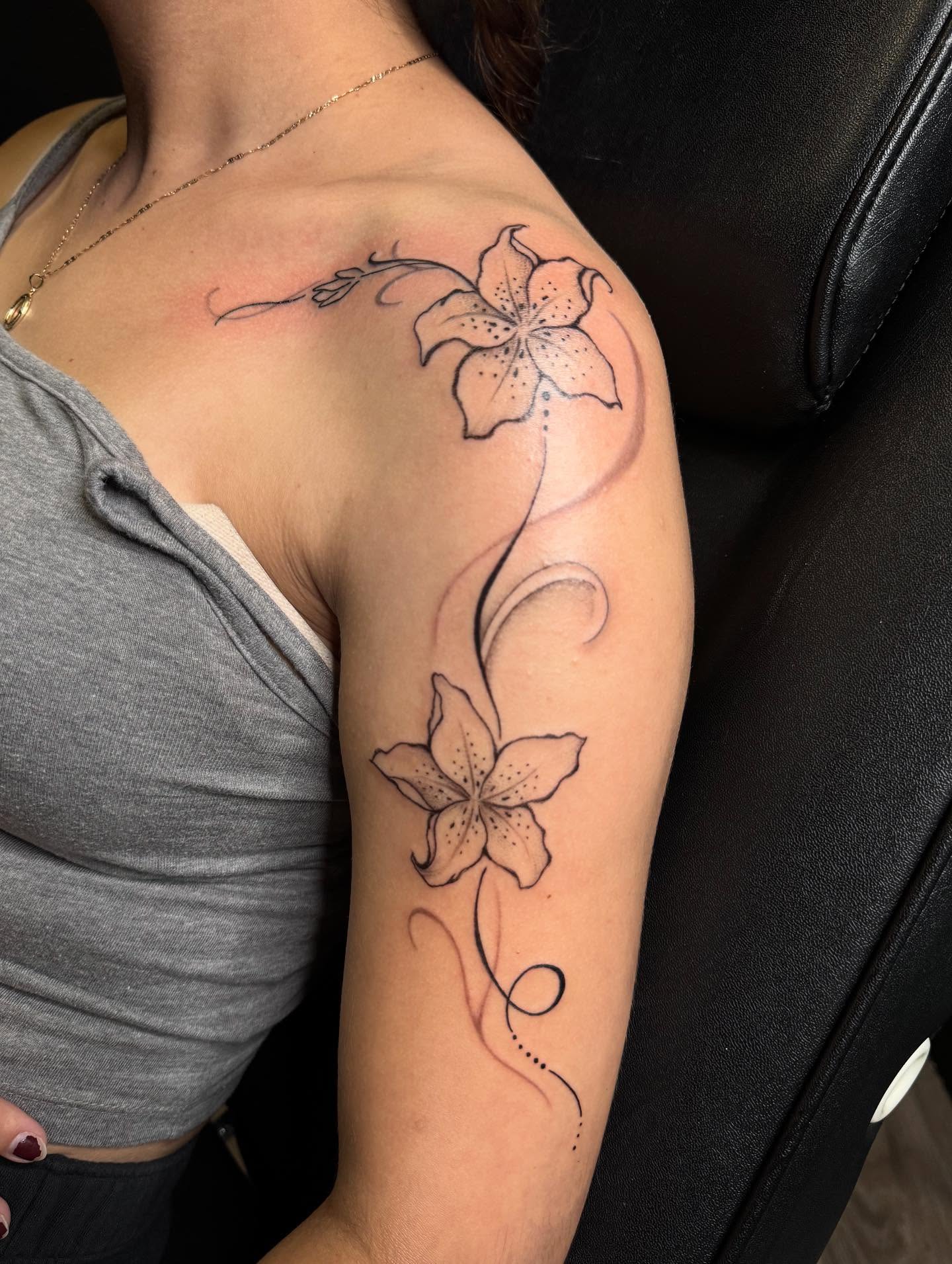 Lily flowers black and grey tattoo on the upper arm by Mickey