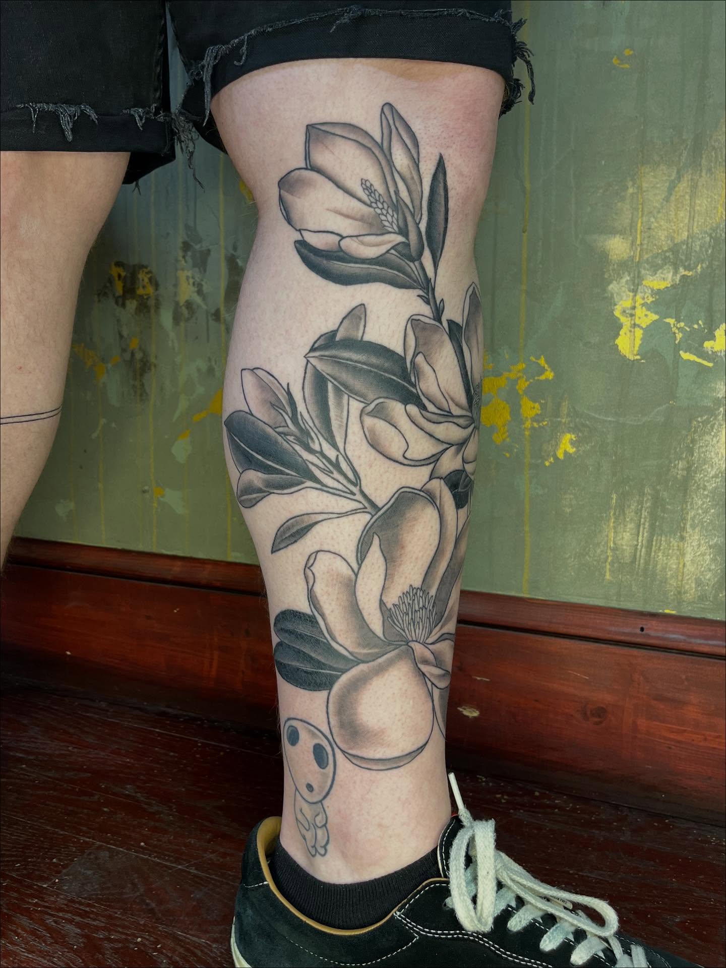 Magnolia flowers black and grey tattoo on the calf by Riley McDonald
