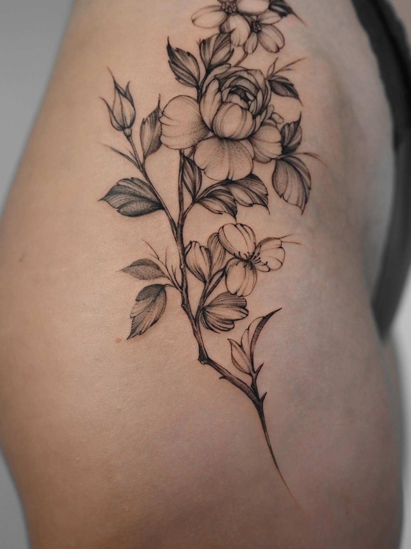 Flower branch black and grey tattoo on the thigh by Anastasiia