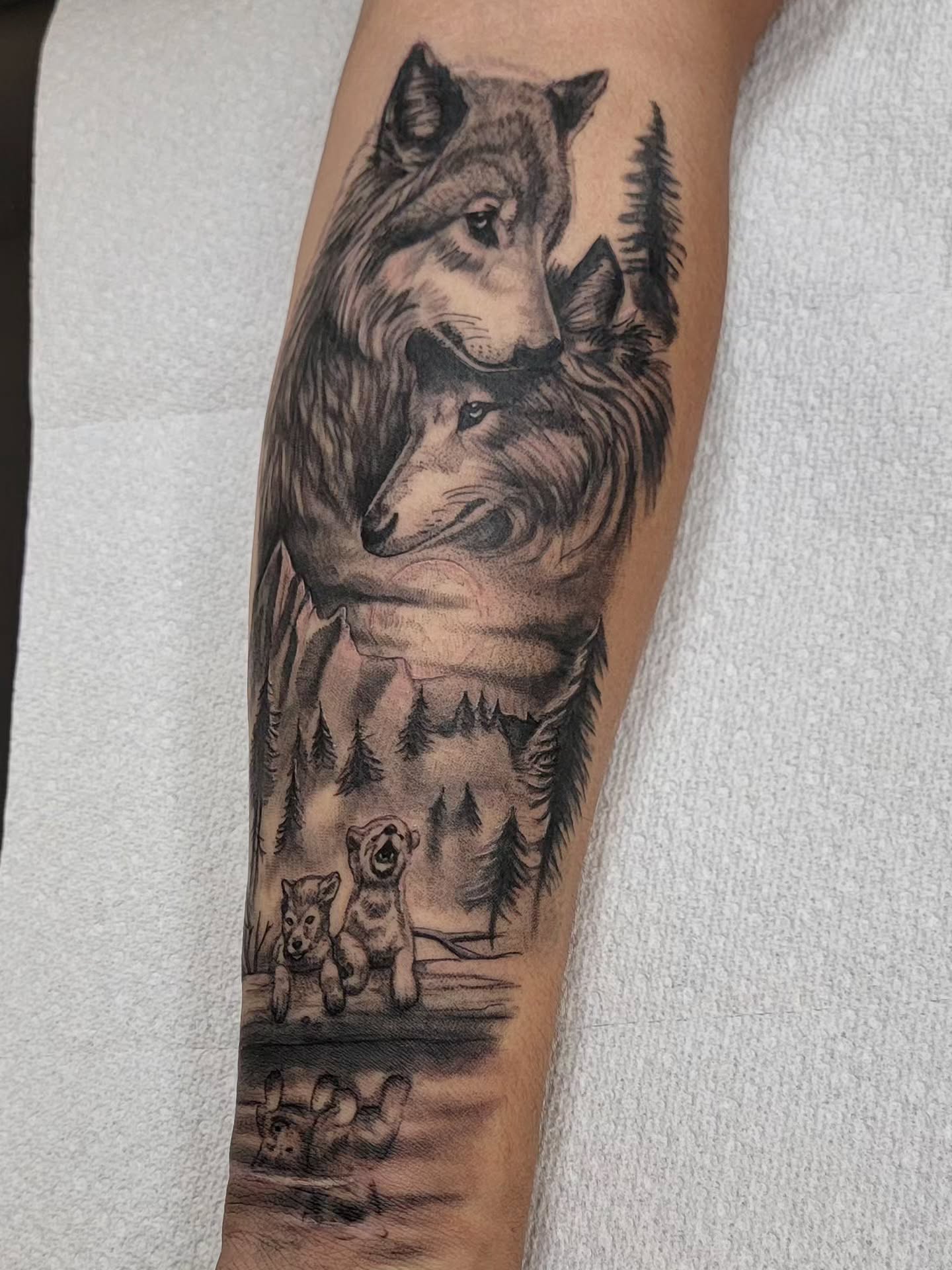 Wolves and cubs in forest landscape realism tattoo on the forearm by Hatchetfoot Art