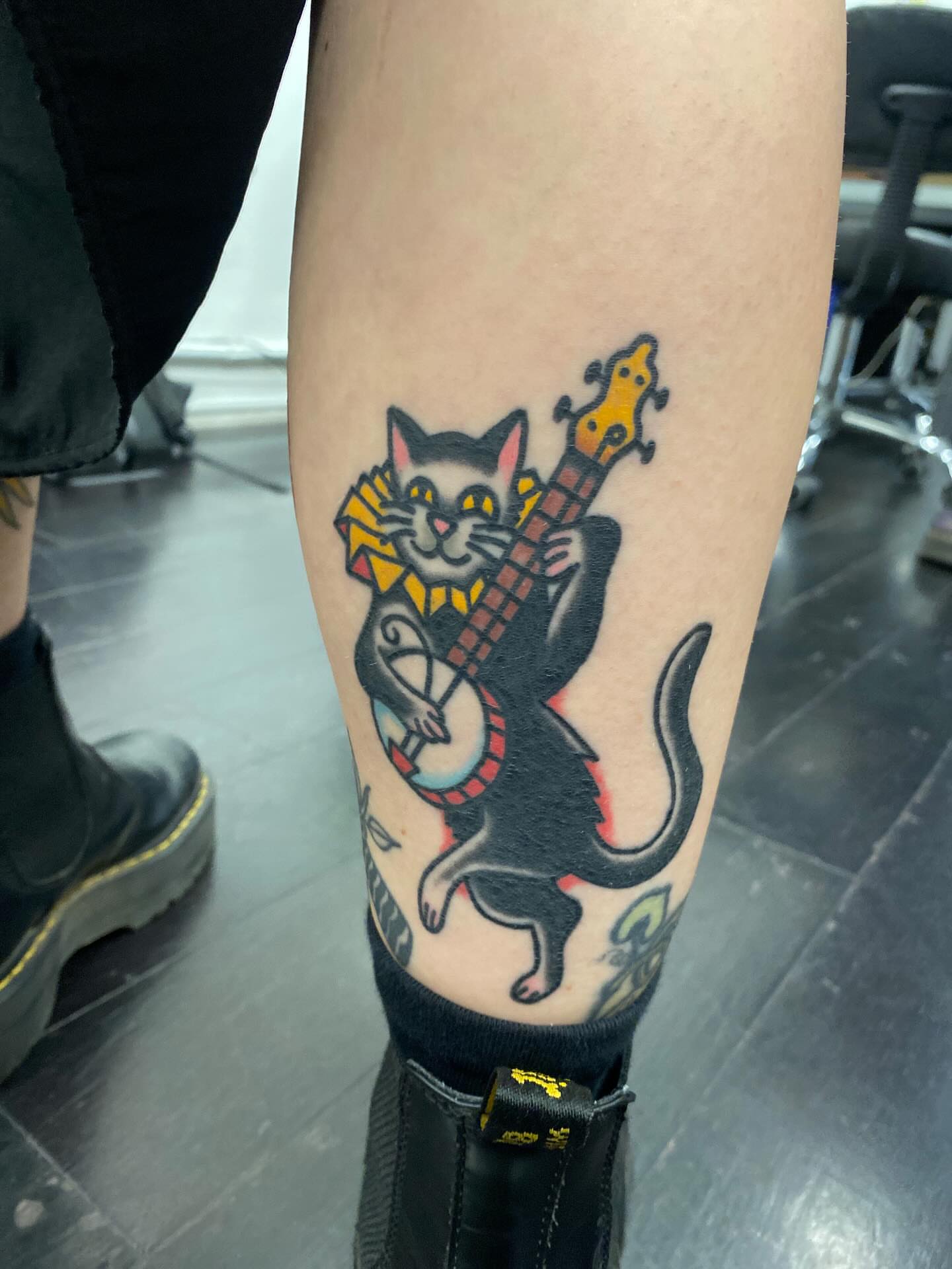 Cat playing banjo American traditional tattoo on the forearm by @rubber_band_dan, San Francisco, California