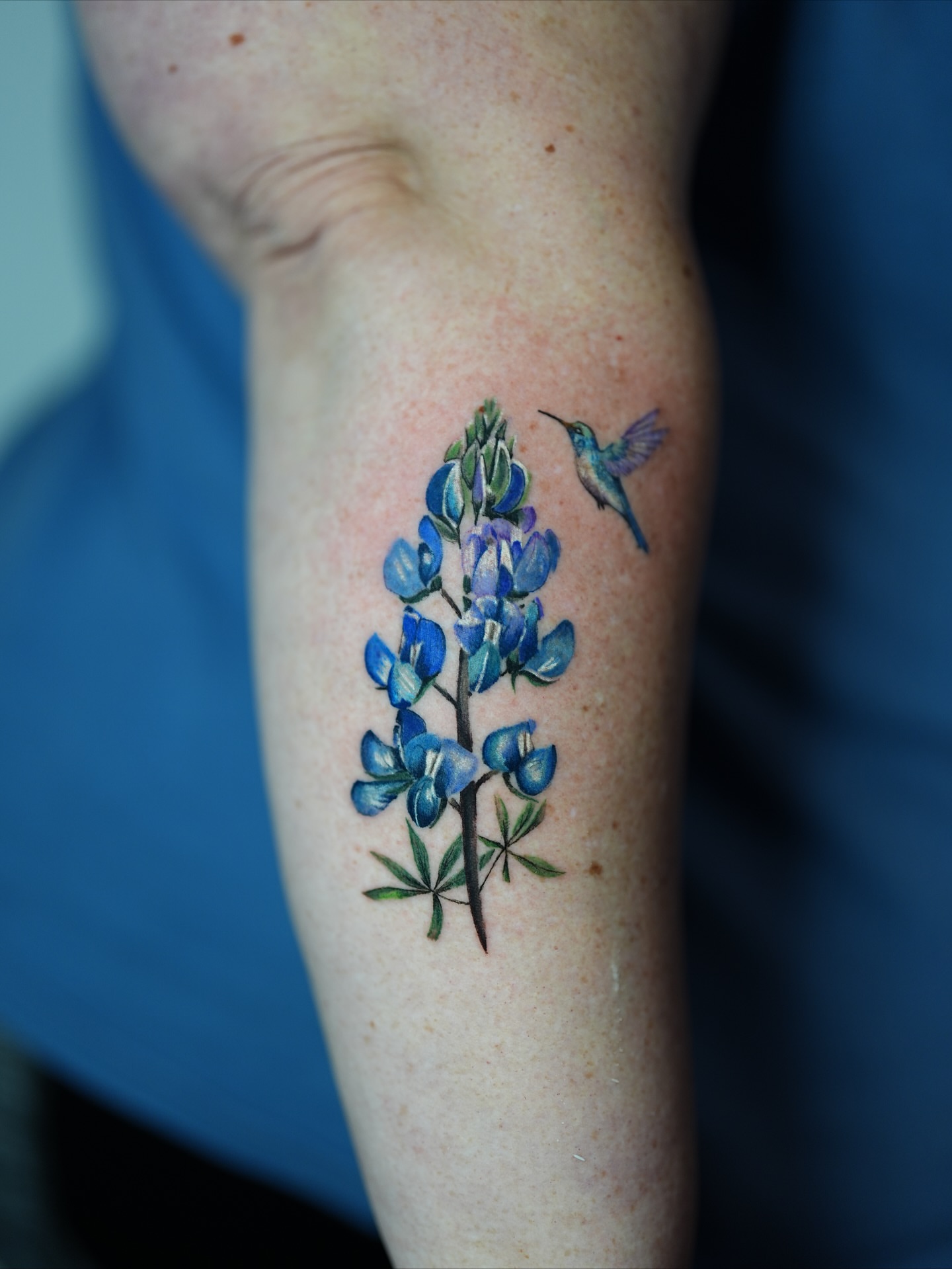Bluebonnet and hummingbird watercolor tattoo on the forearm by Henry