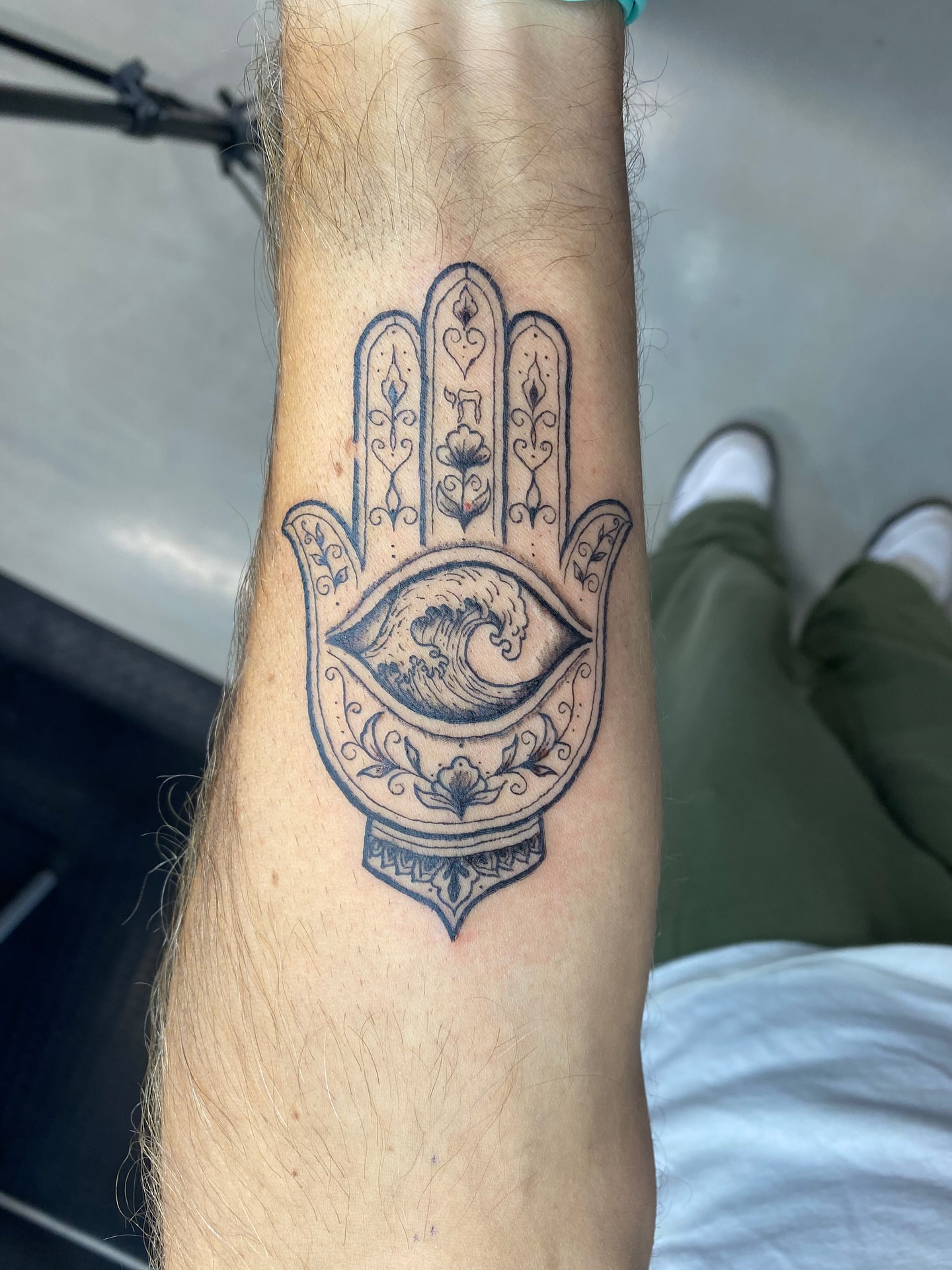 Hamsa hand with eye black and grey tattoo on the forearm by Ellena Reggiani