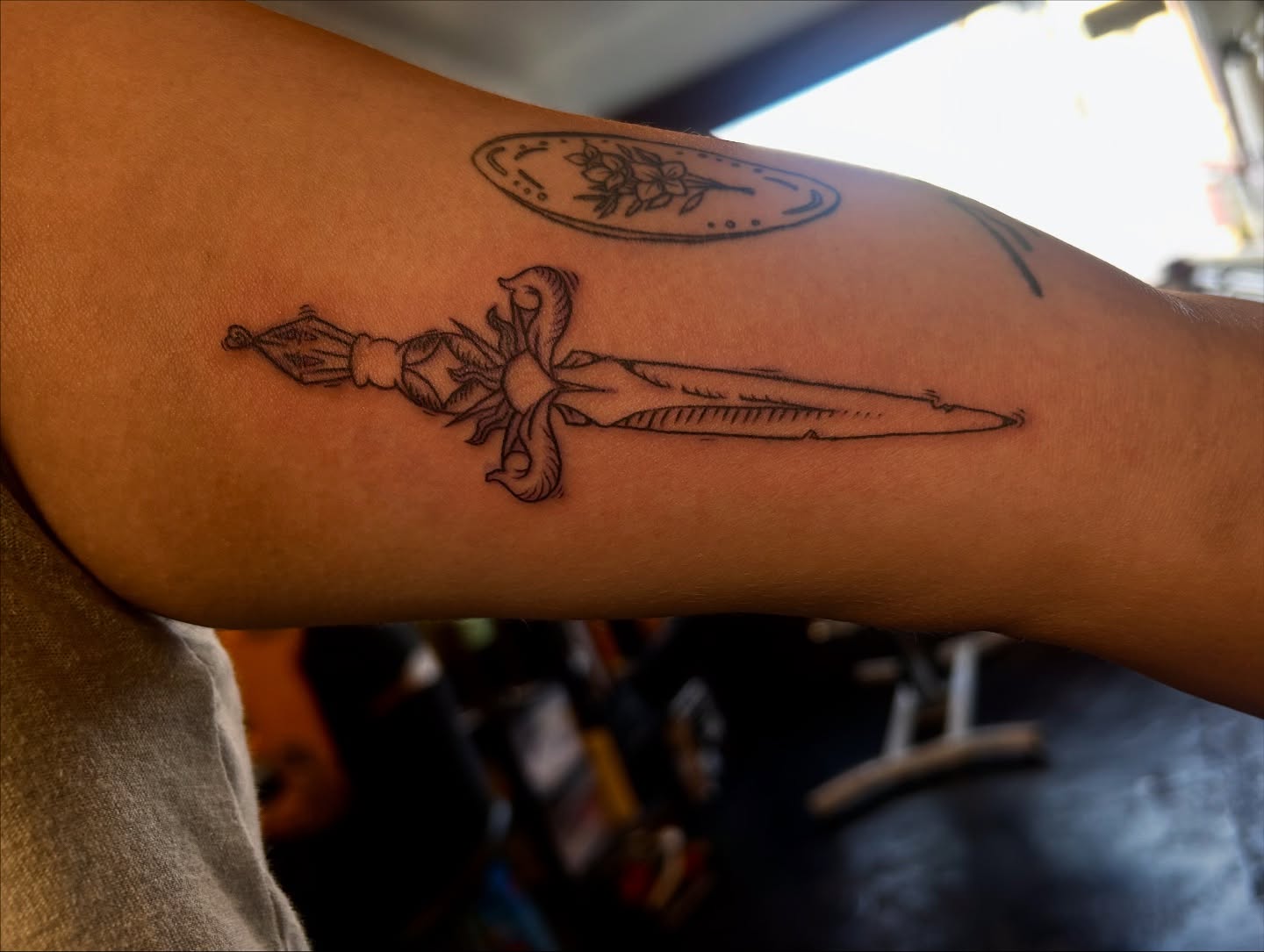 Sword and bow black and grey tattoo on the forearm by King By Trade 👑