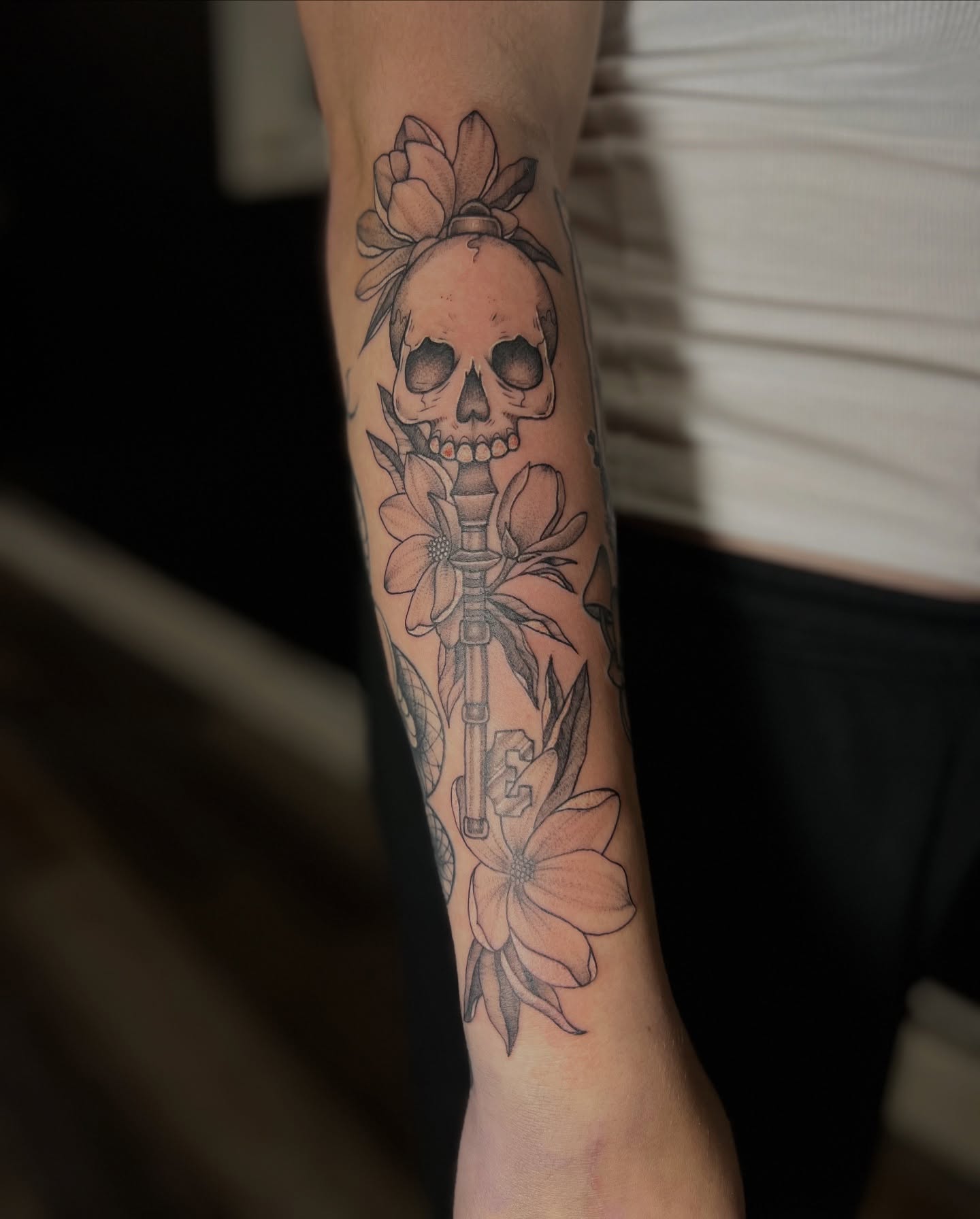 Skull with flowers black and grey tattoo on the forearm by Lauren