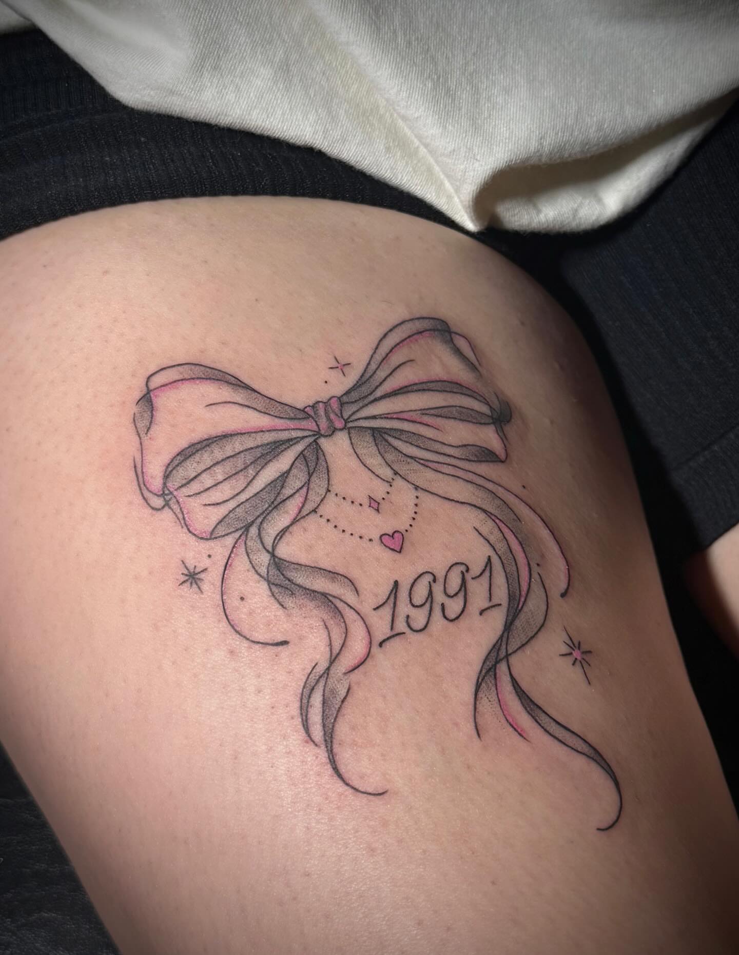 Bow and ribbon black and grey tattoo on the thigh by abbie michelle