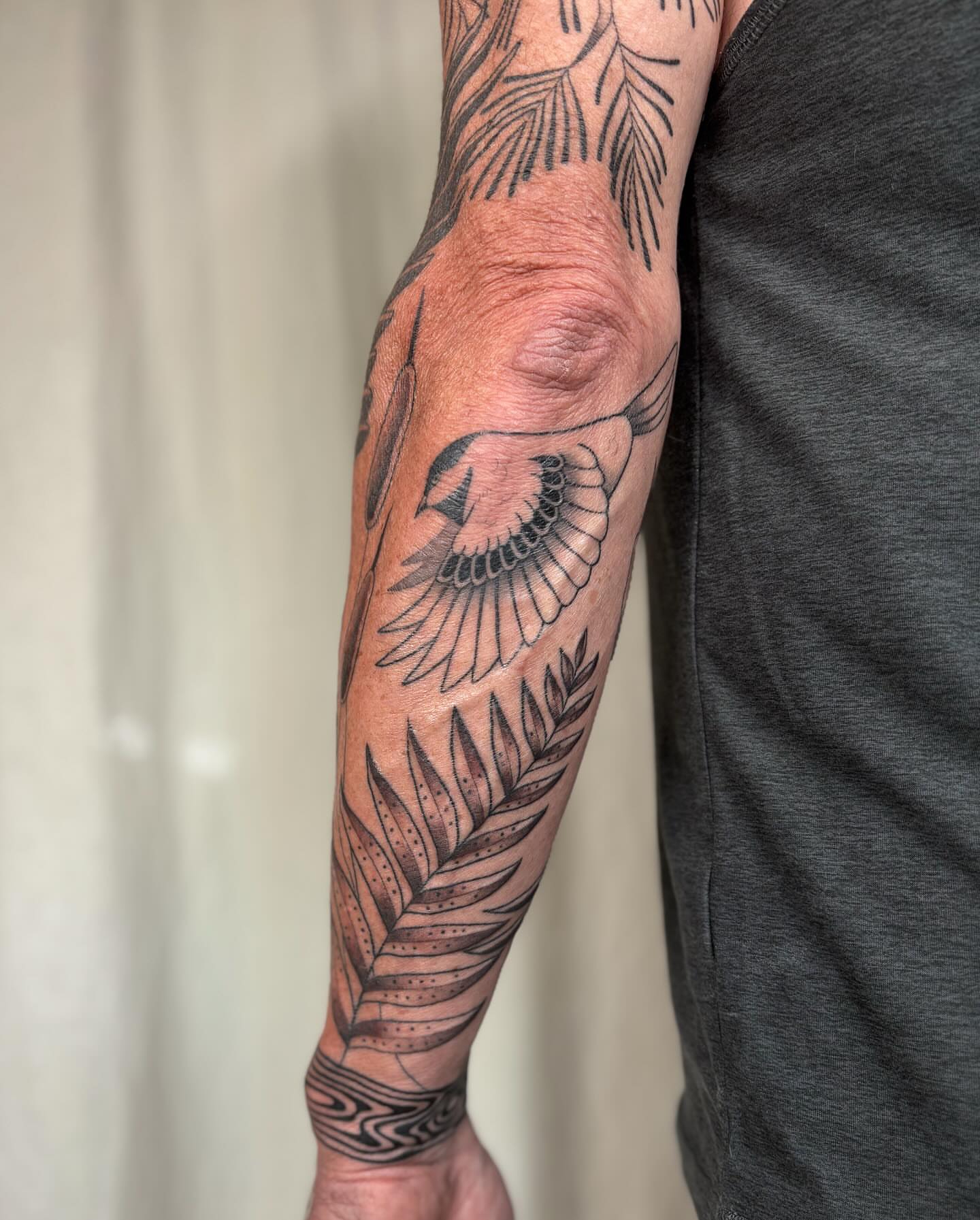 Bird and fern black and grey tattoo on the forearm by Anna Sage