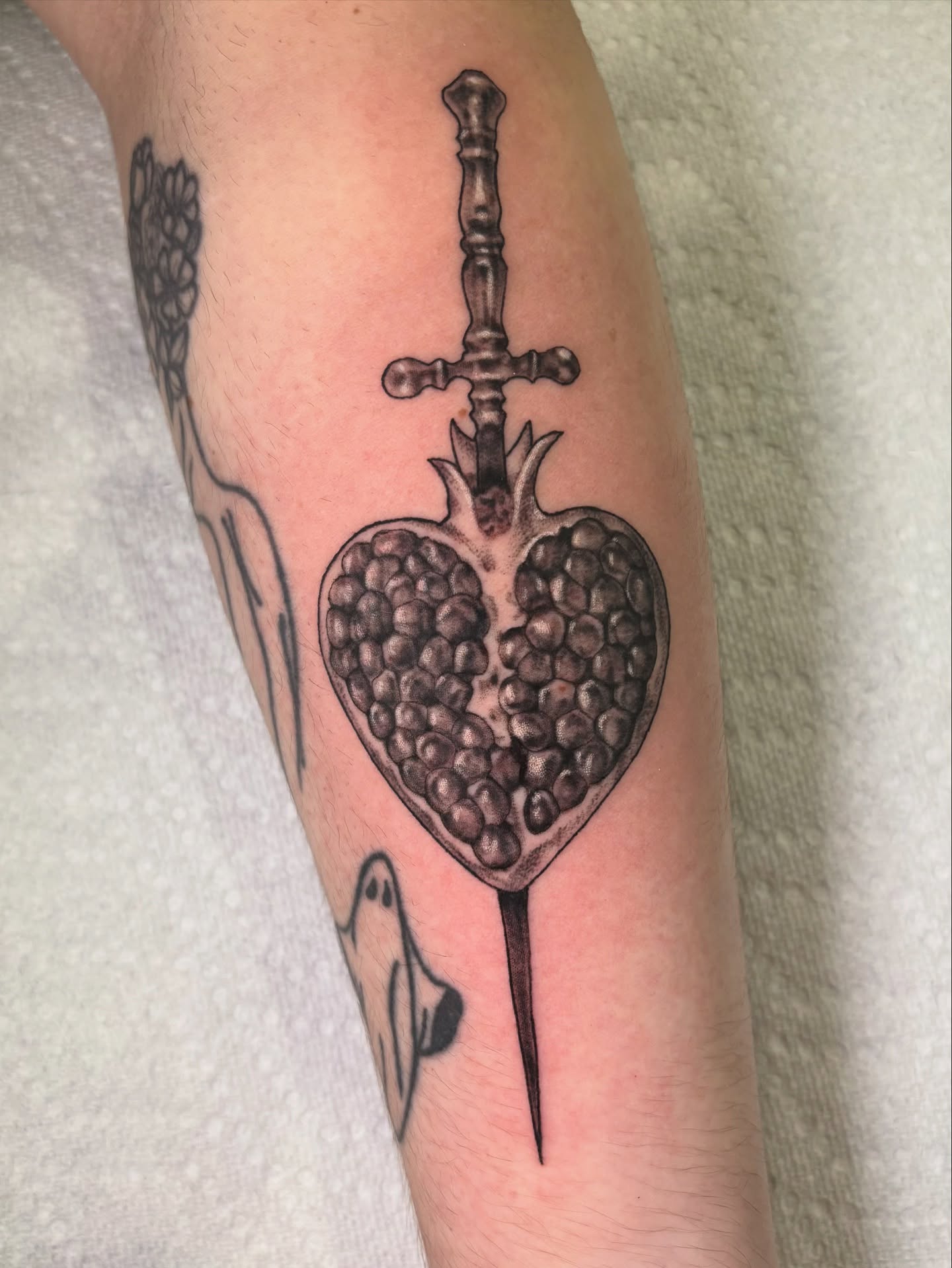 Heart with pomegranate seeds black and grey tattoo on the forearm by Flor, Dallas, Texas