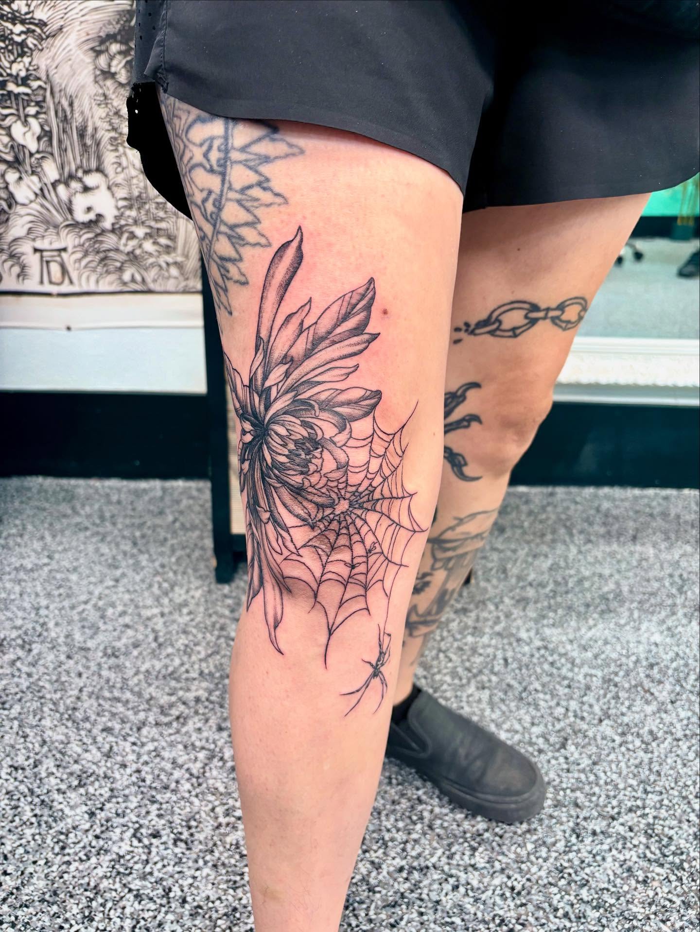 Flower and spiderweb black and grey tattoo on the thigh by Jayda Shell