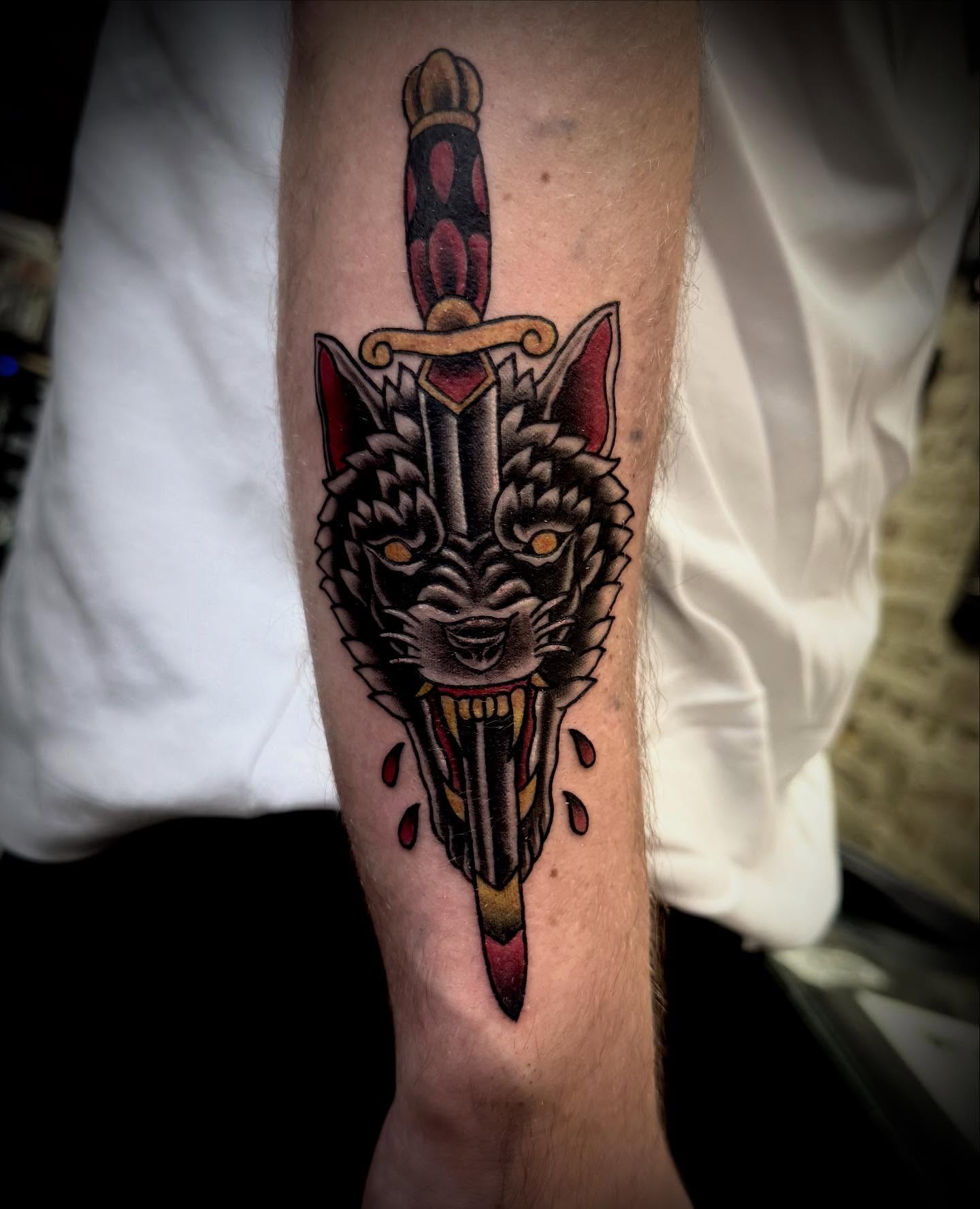 Wolf head with dagger American traditional tattoo on the forearm by Jameson William Cowan