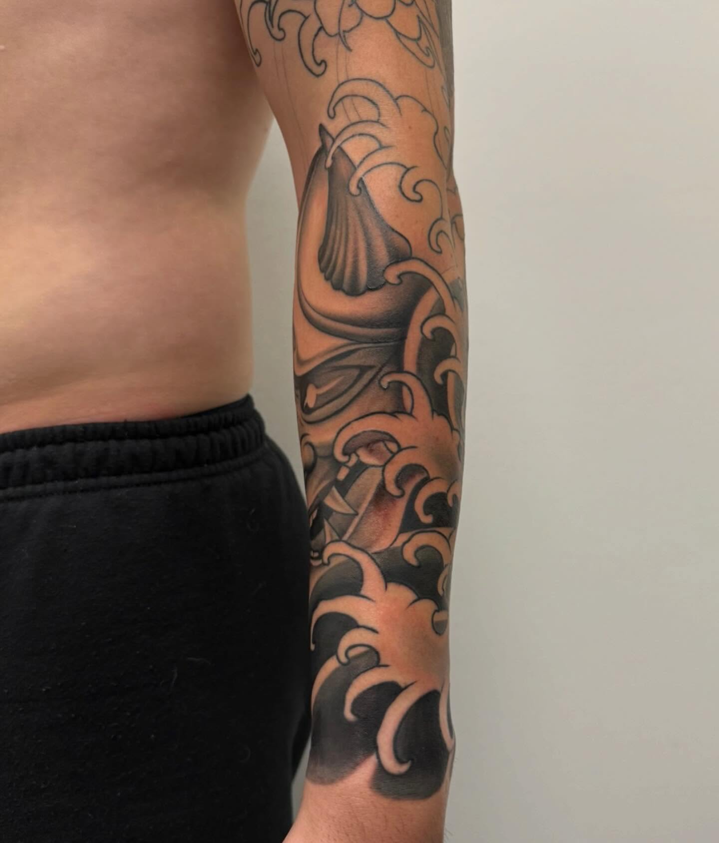 Waves and shell black and grey tattoo on the forearm by Sam Oakes