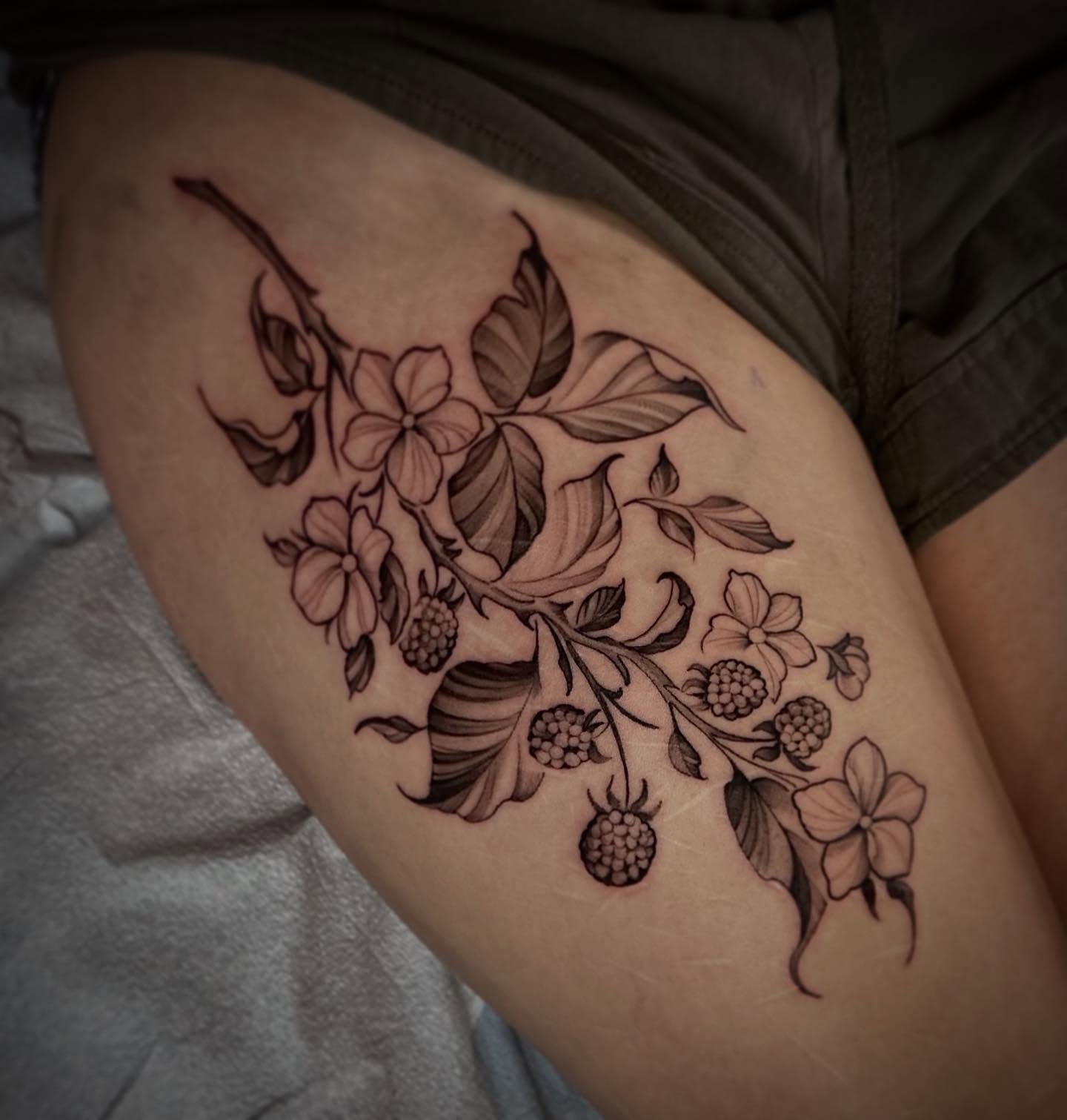 Flower and berry branch black and grey tattoo on the thigh by Sebastian Livingston